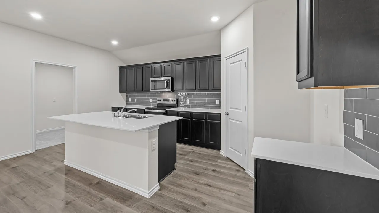 Kitchen featuring a central island with a sink, dark wood-finish cabinetry, light-toned countertops, stainless steel appliances, and a gray subway tile backsplash
