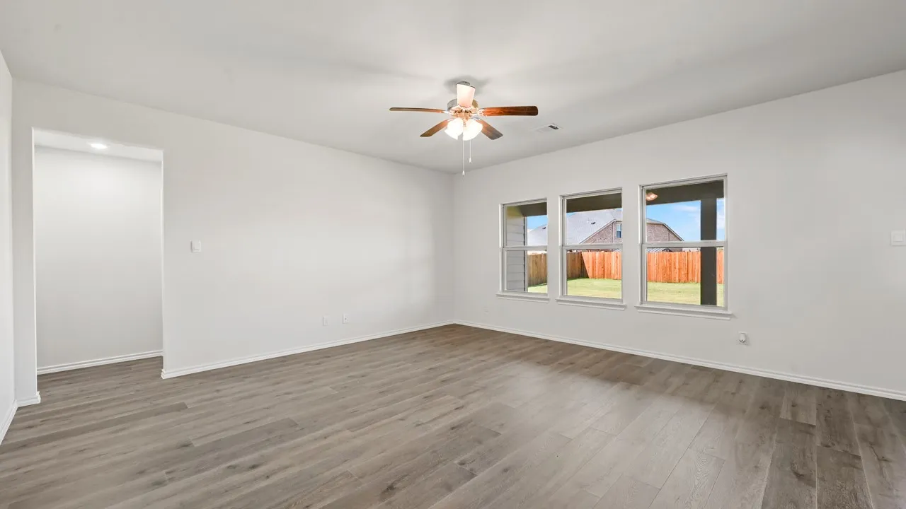 Spacious room featuring wood-finish flooring, white walls, and a ceiling fan