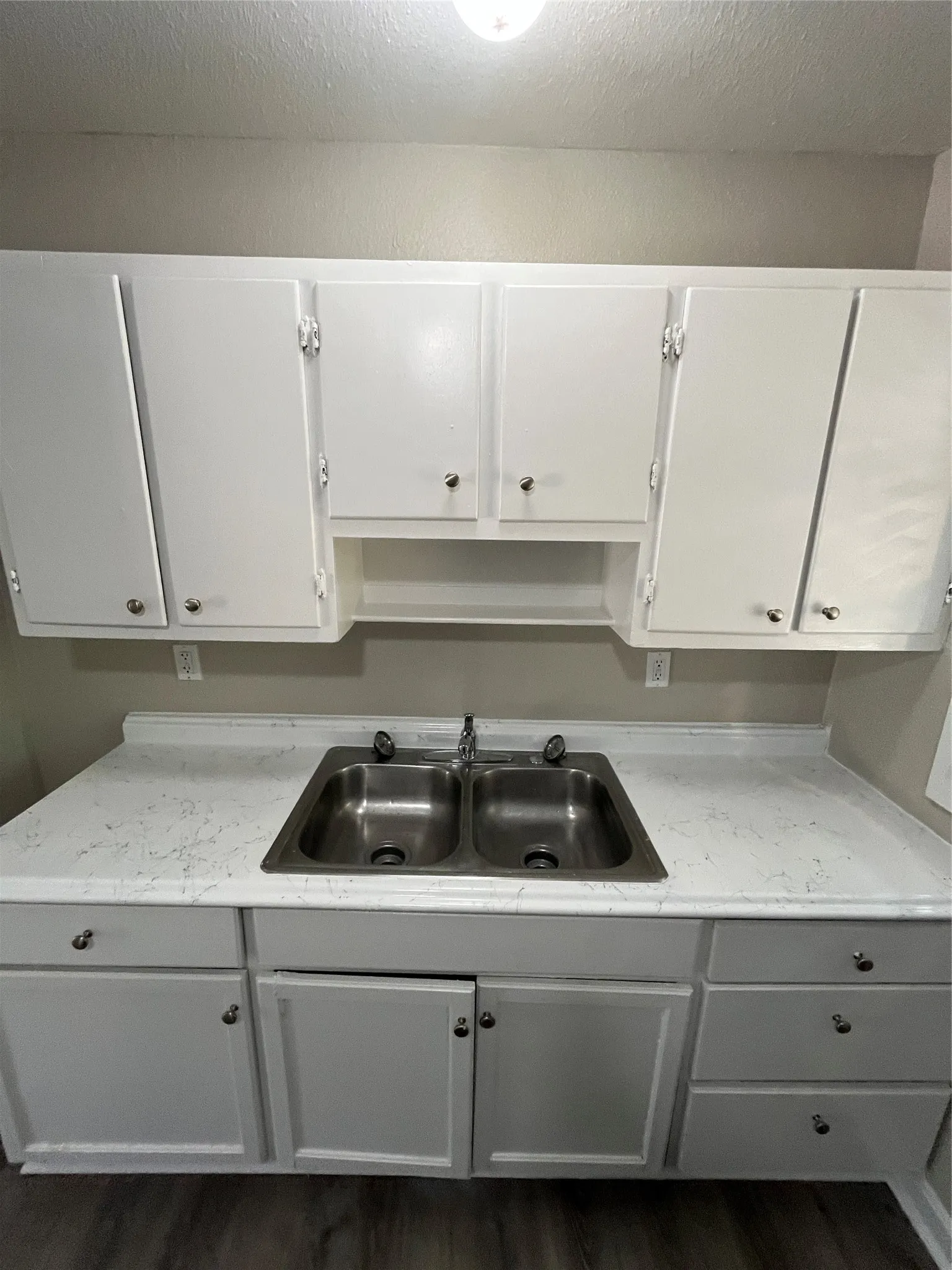 Galley kitchen with white cabinetry, stainless steel double basin sink, light-toned countertops, and wood-finish flooring