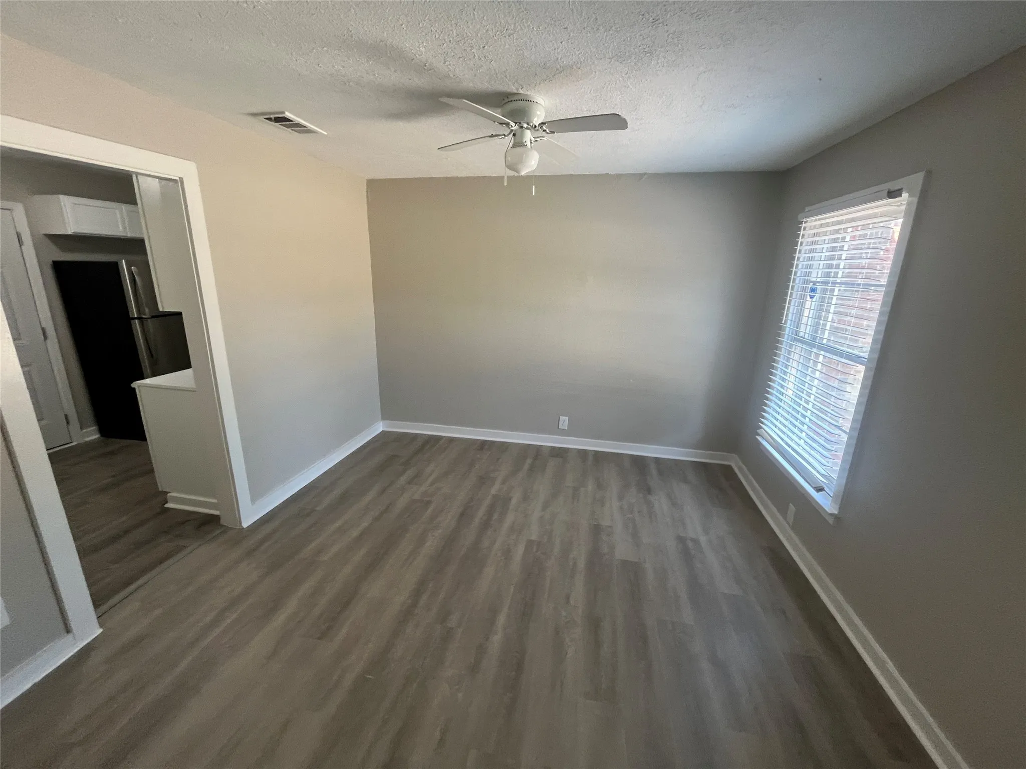 Wood-finish flooring, neutral wall tones, window with horizontal blinds, and a ceiling fan with integrated lighting
