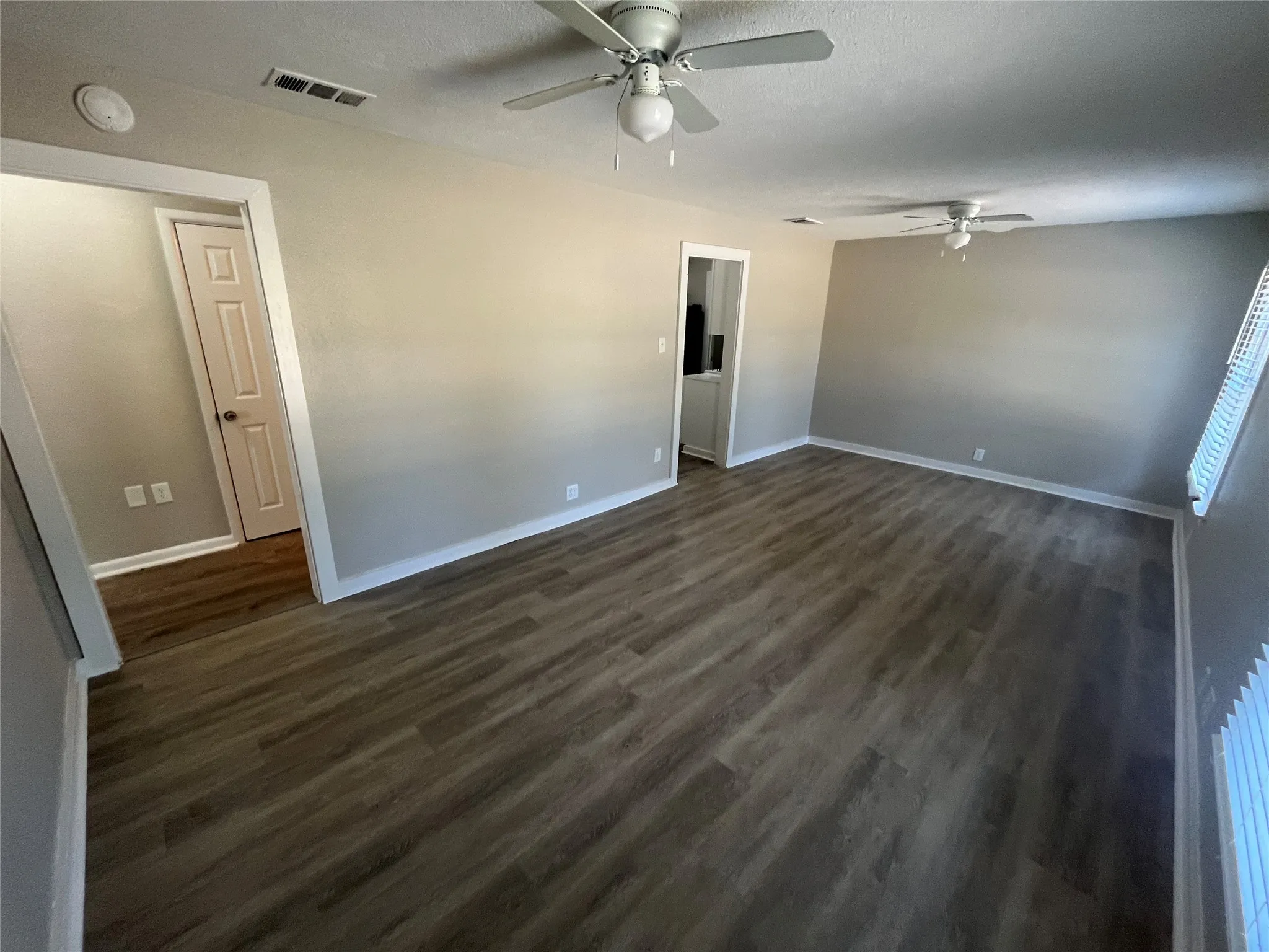 Spacious room featuring wood-finish flooring, light neutral wall tones, white trim, and two ceiling fans