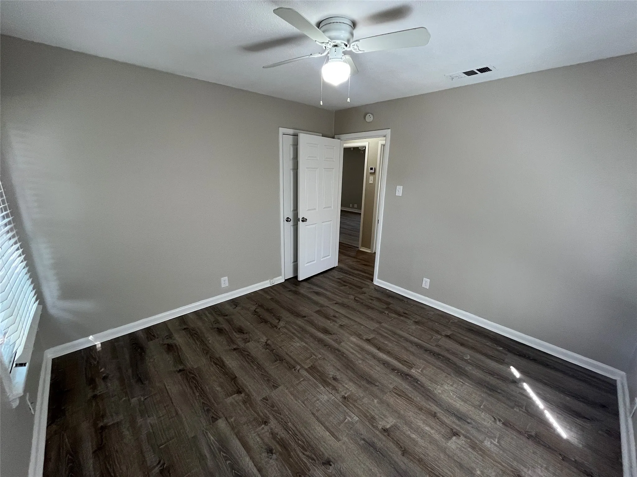 Wood-finish flooring, light gray wall color, white ceiling fan, and window with horizontal blinds
