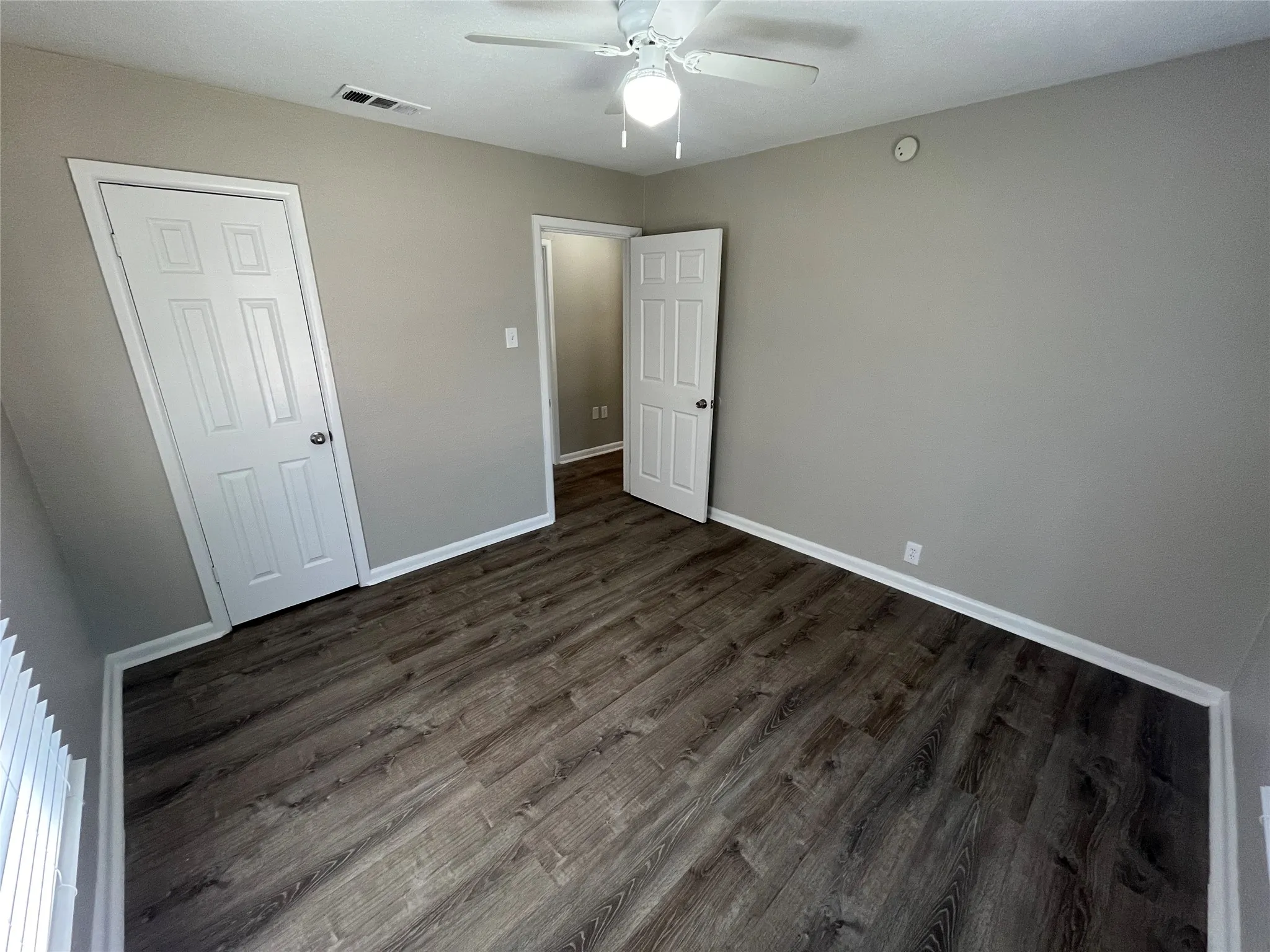 Wood-finish flooring, neutral gray wall tones, white trim, paneled doors, and a ceiling fan with integrated lighting