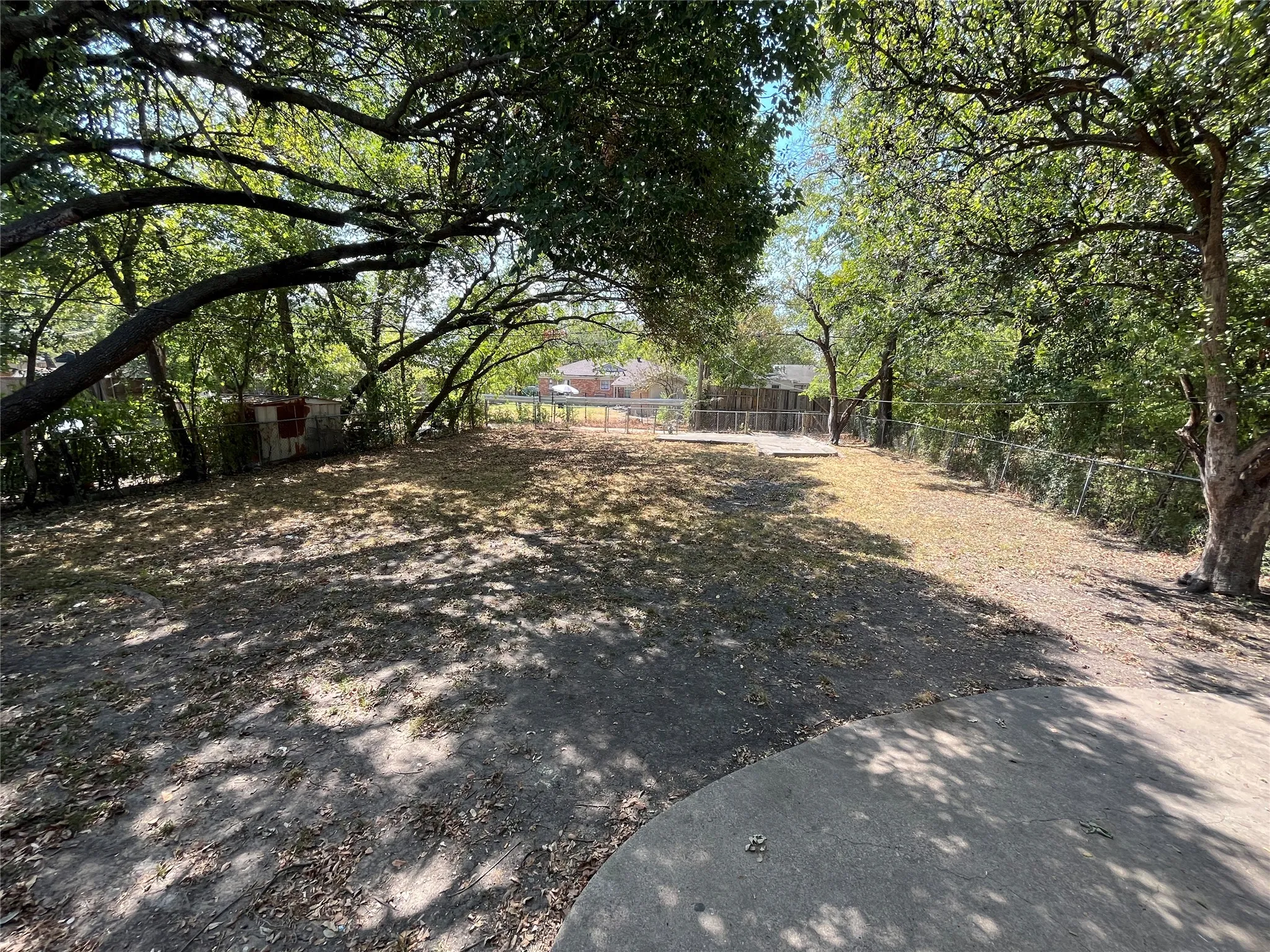 Expansive outdoor space featuring mature trees, a concrete patio, and chain-link fencing