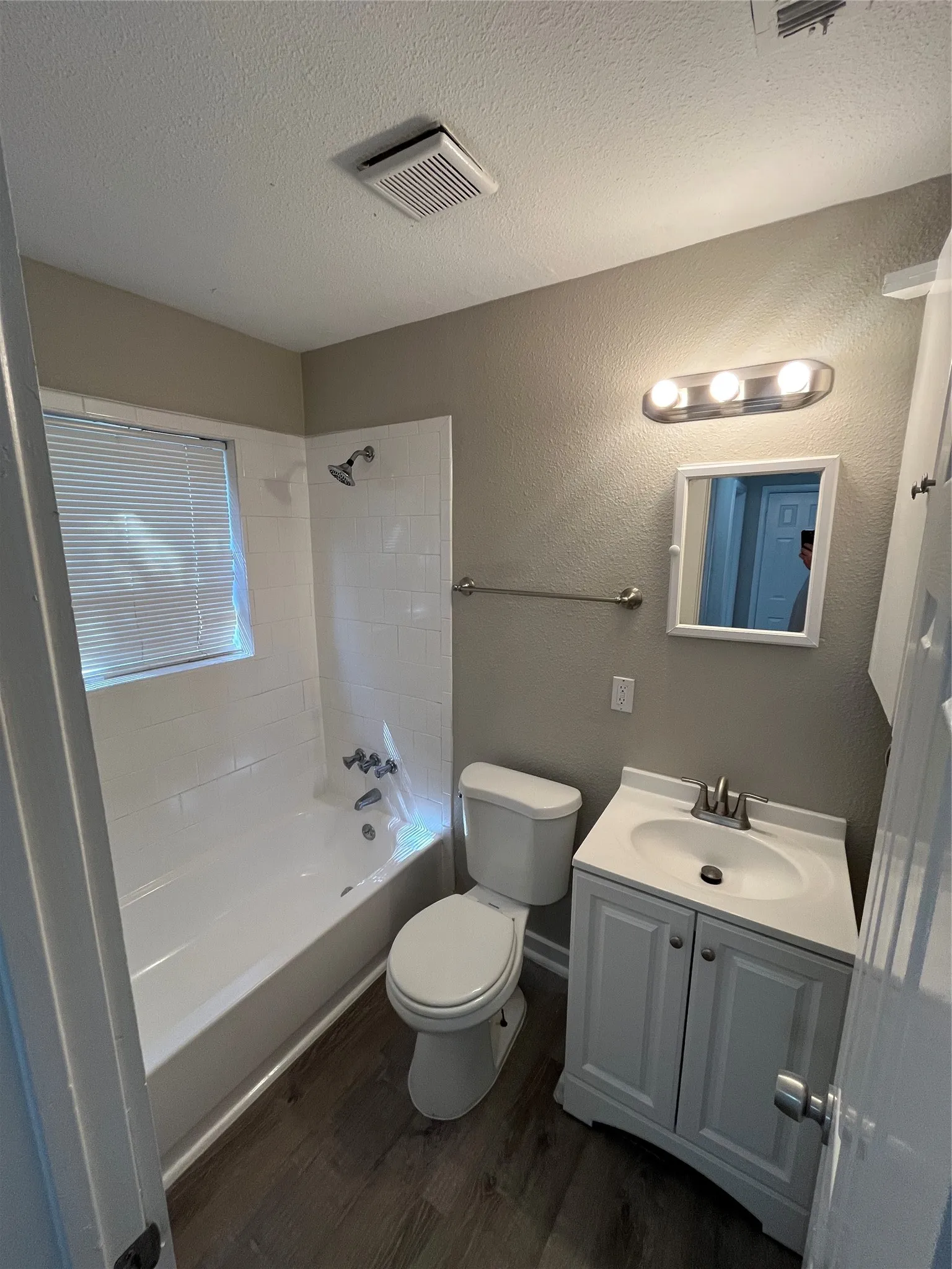 Bathroom featuring a white bathtub with subway tile surround, white vanity with integrated sink, wood-finish flooring, and a window with horizontal blinds