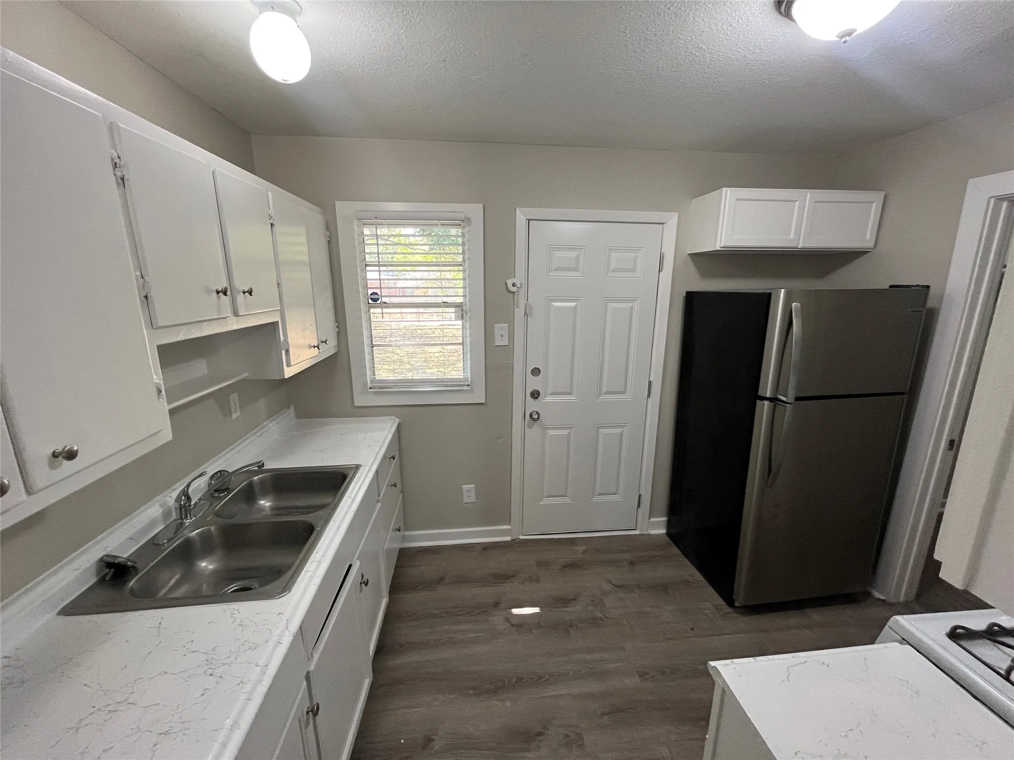 Kitchen featuring white cabinetry, wood-finish flooring, a double basin stainless steel sink, and light-colored countertops