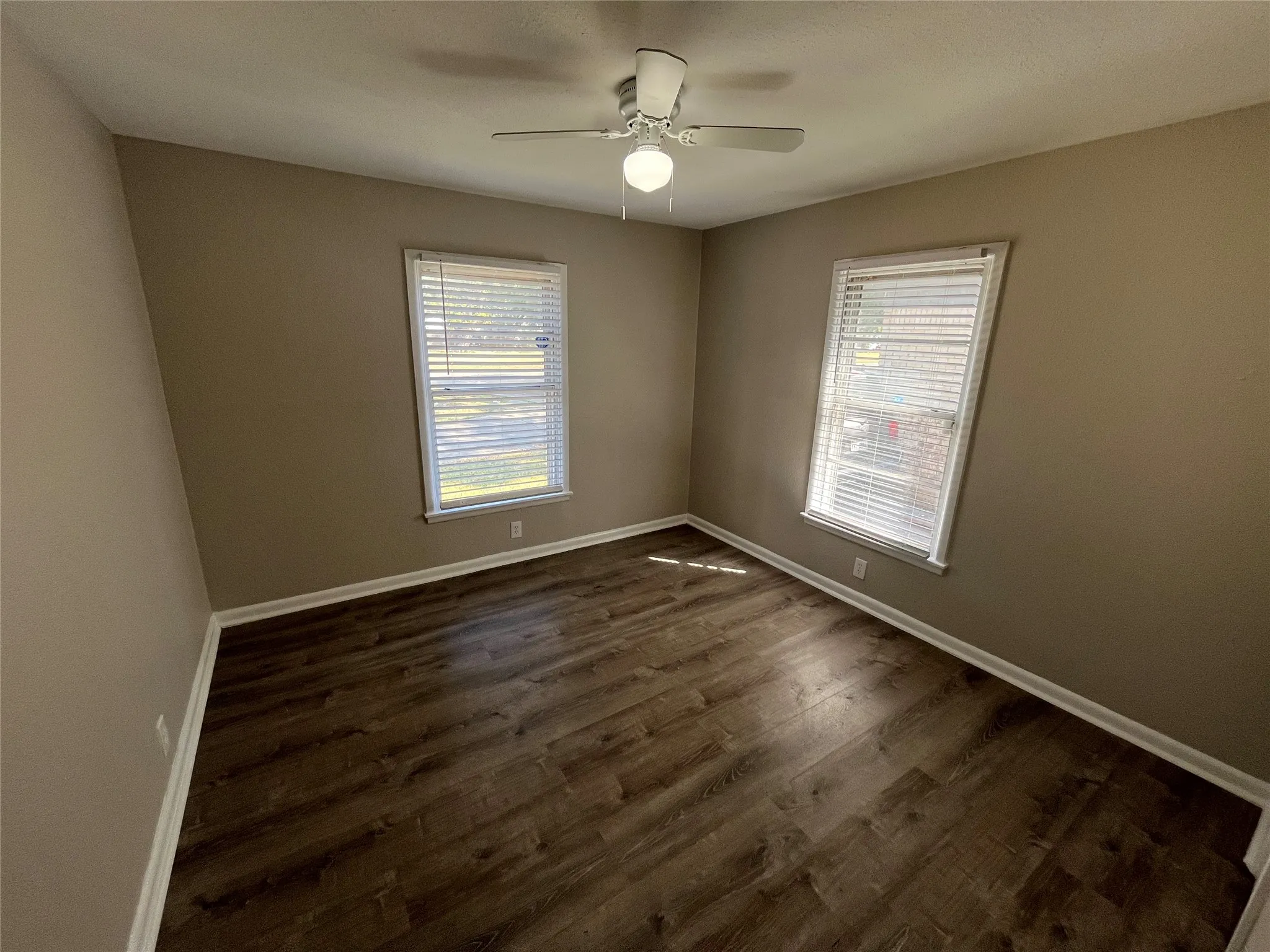Wood-finish flooring, two windows with blinds, and a ceiling fan with integrated lighting