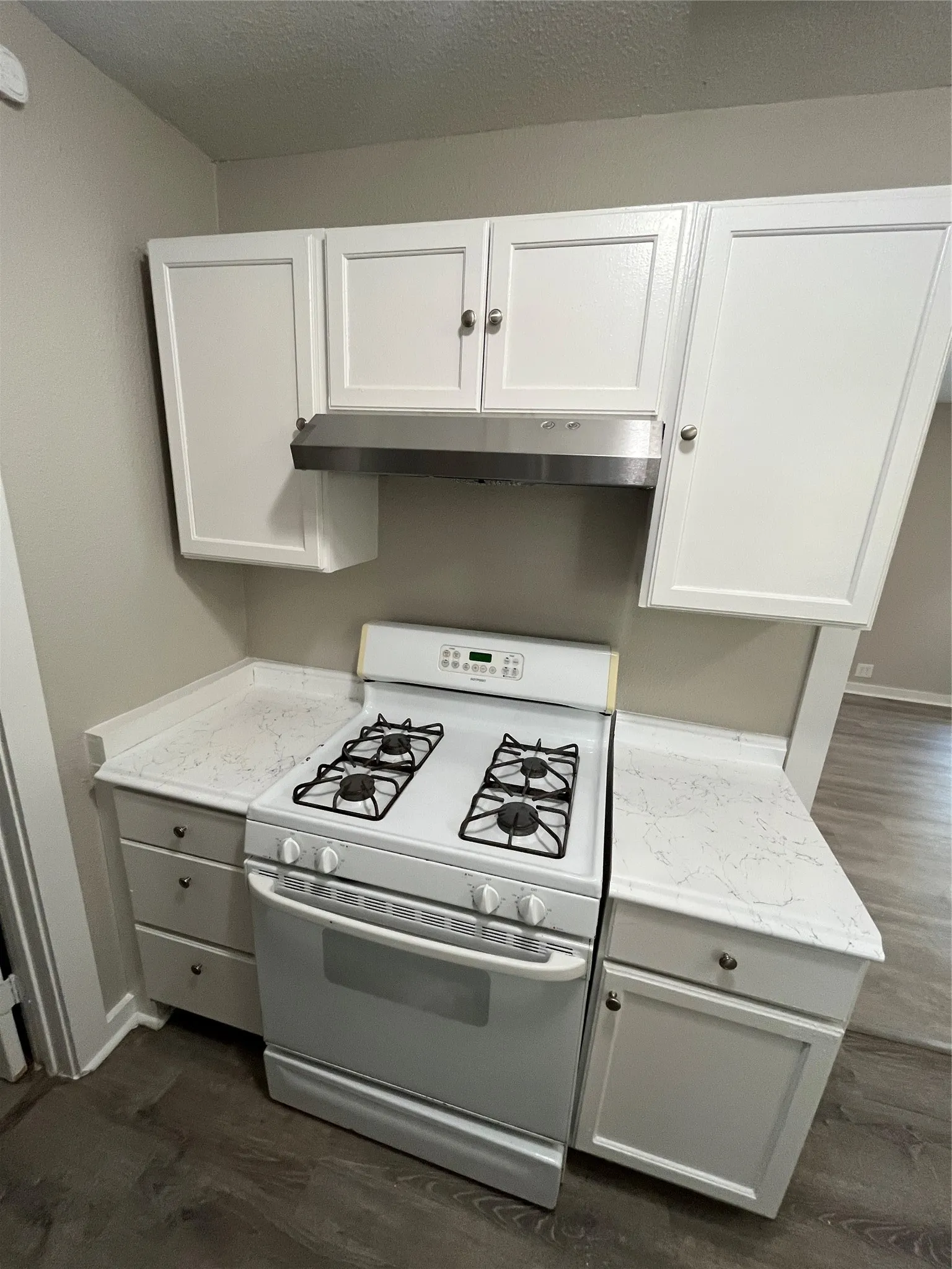 White shaker-style cabinetry with silver-tone hardware, white gas range, stainless steel range hood, stone-finish countertops, and wood-finish flooring