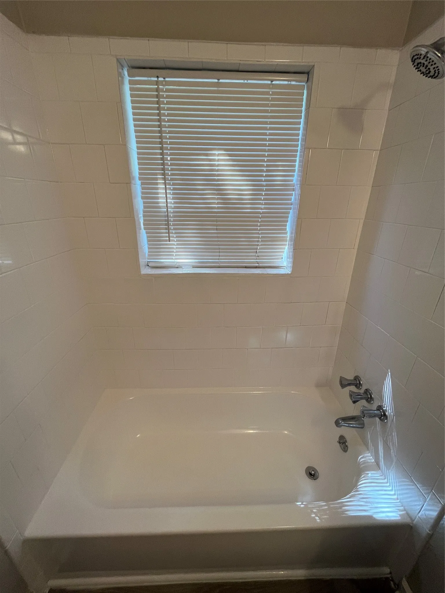 White tiled shower enclosure with a window, white bathtub, and chrome fixtures