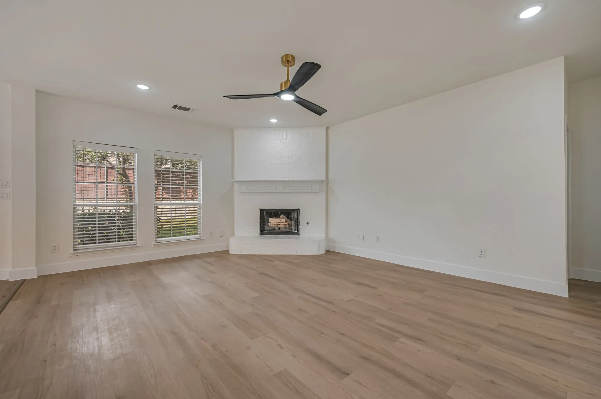 Luxury Vinyl Plank  flooring, brick fireplace with mantel, recessed lighting, ceiling fan, and multiple windows