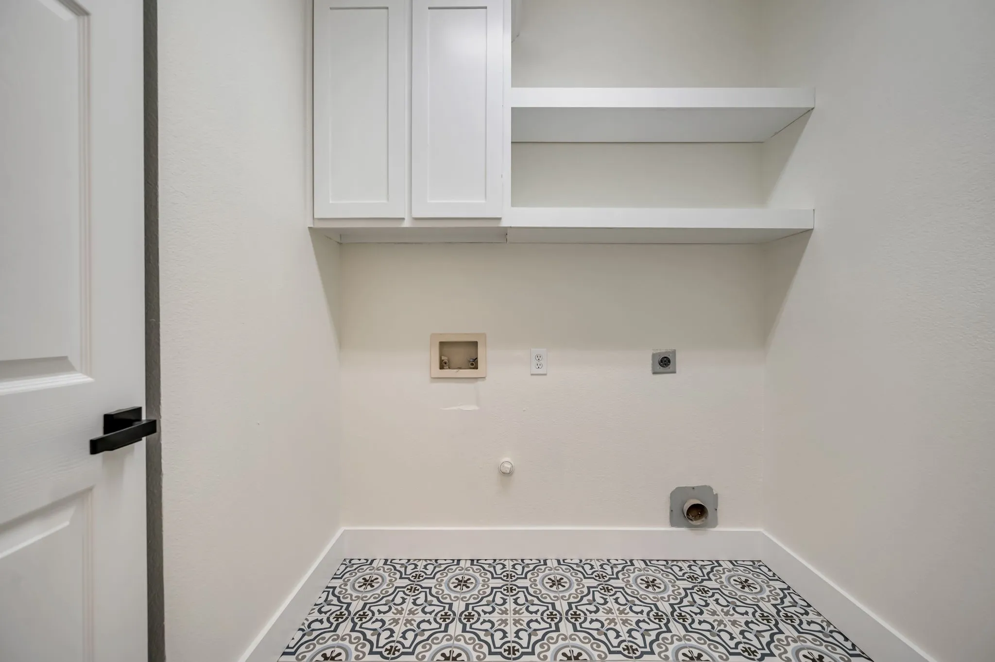 White shaker-style cabinetry, open shelving, white walls, black door hardware, and patterned floor tiling