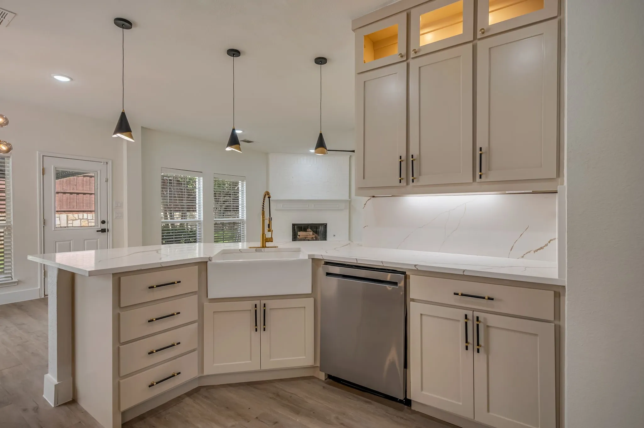 Kitchen with light-toned cabinetry, a farmhouse sink, stainless steel dishwasher, Quartz countertops with gold veining, and pendant lighting