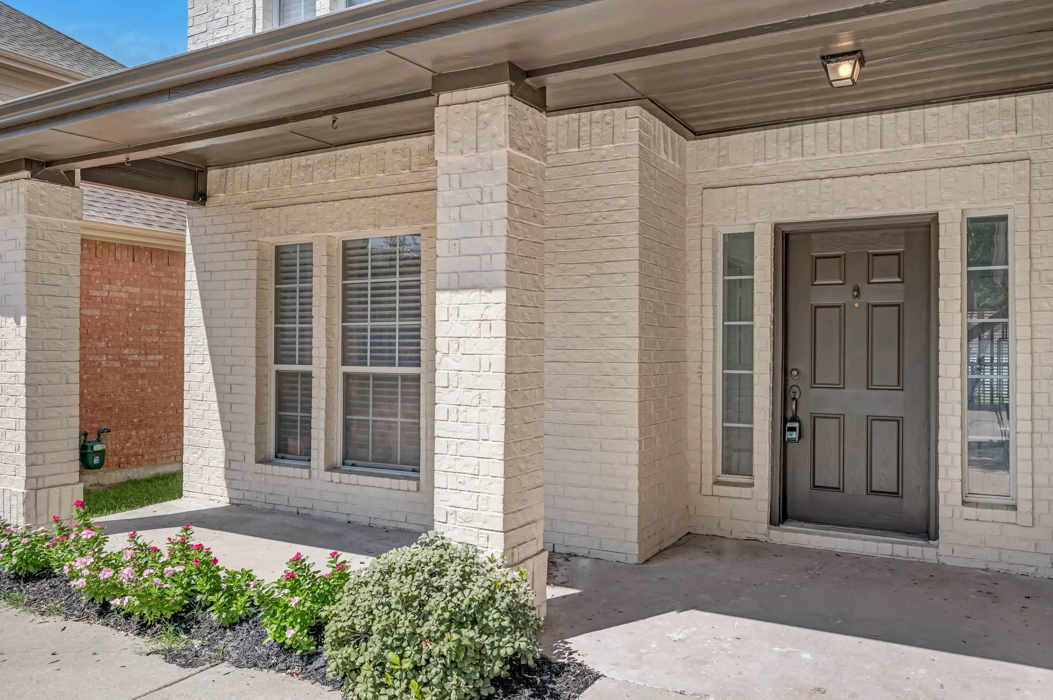 Cream-colored brick exterior with a covered porch, recessed lighting, and a dark paneled entry door