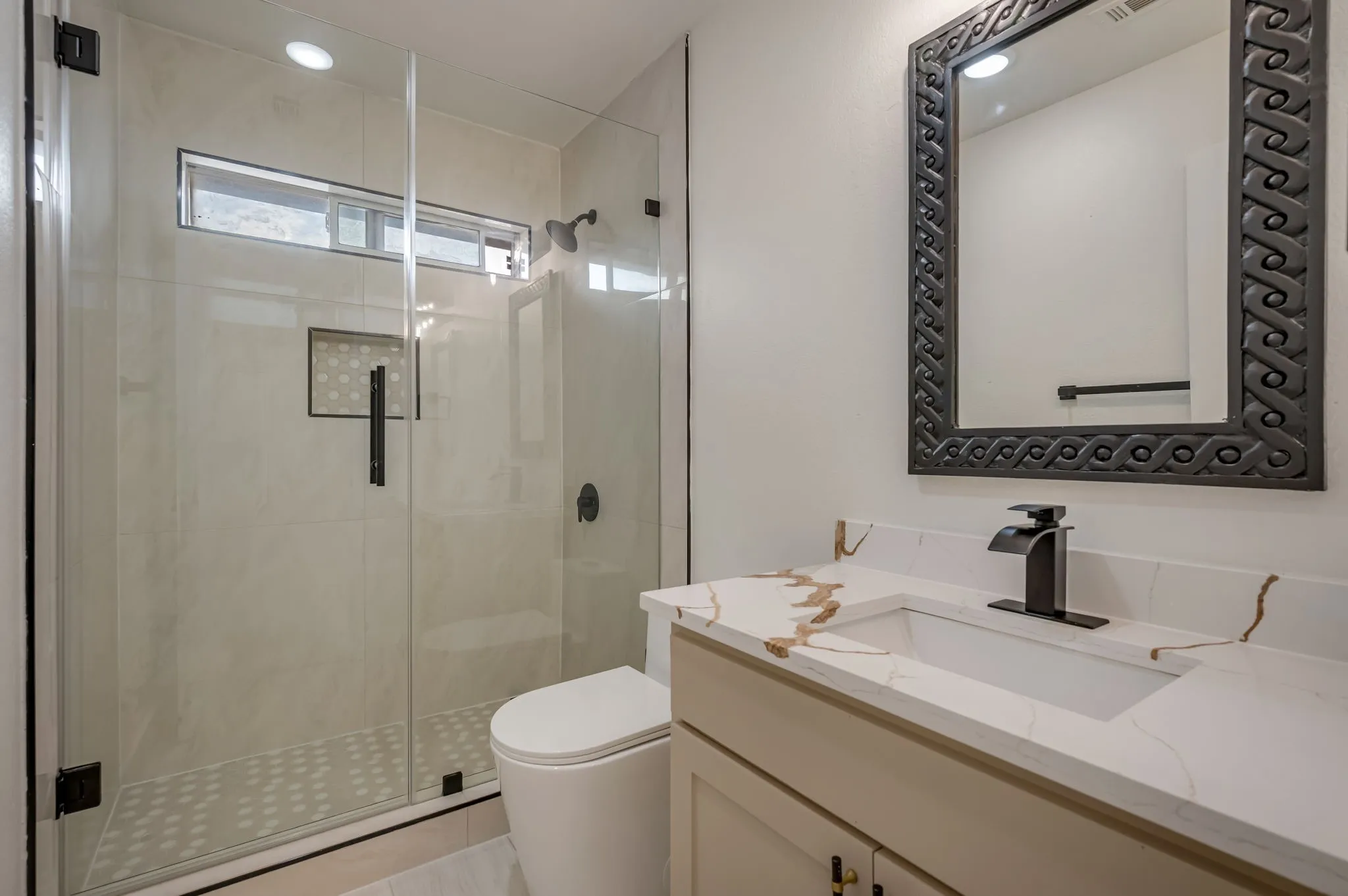 Walk-in shower with clear glass enclosure, transom window, and tiled accent niche