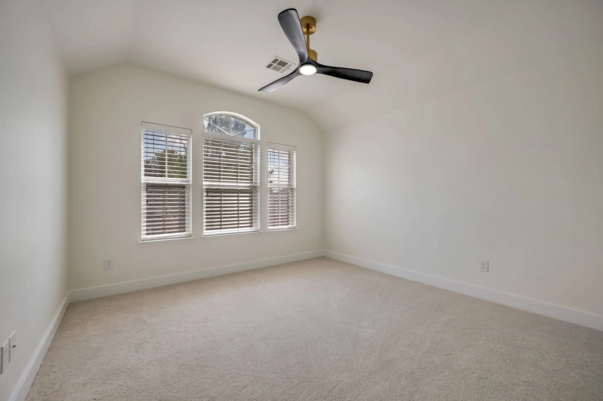 Vaulted ceiling, arched window detail, light-colored carpeting, multiple windows with blinds, and a modern ceiling fan