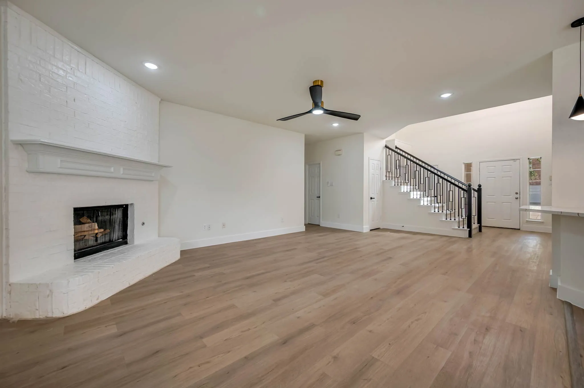 Spacious living area featuring Luxury Vinyl Plank  flooring, a white-painted brick fireplace with mantel, a modern ceiling fan, and recessed lighting