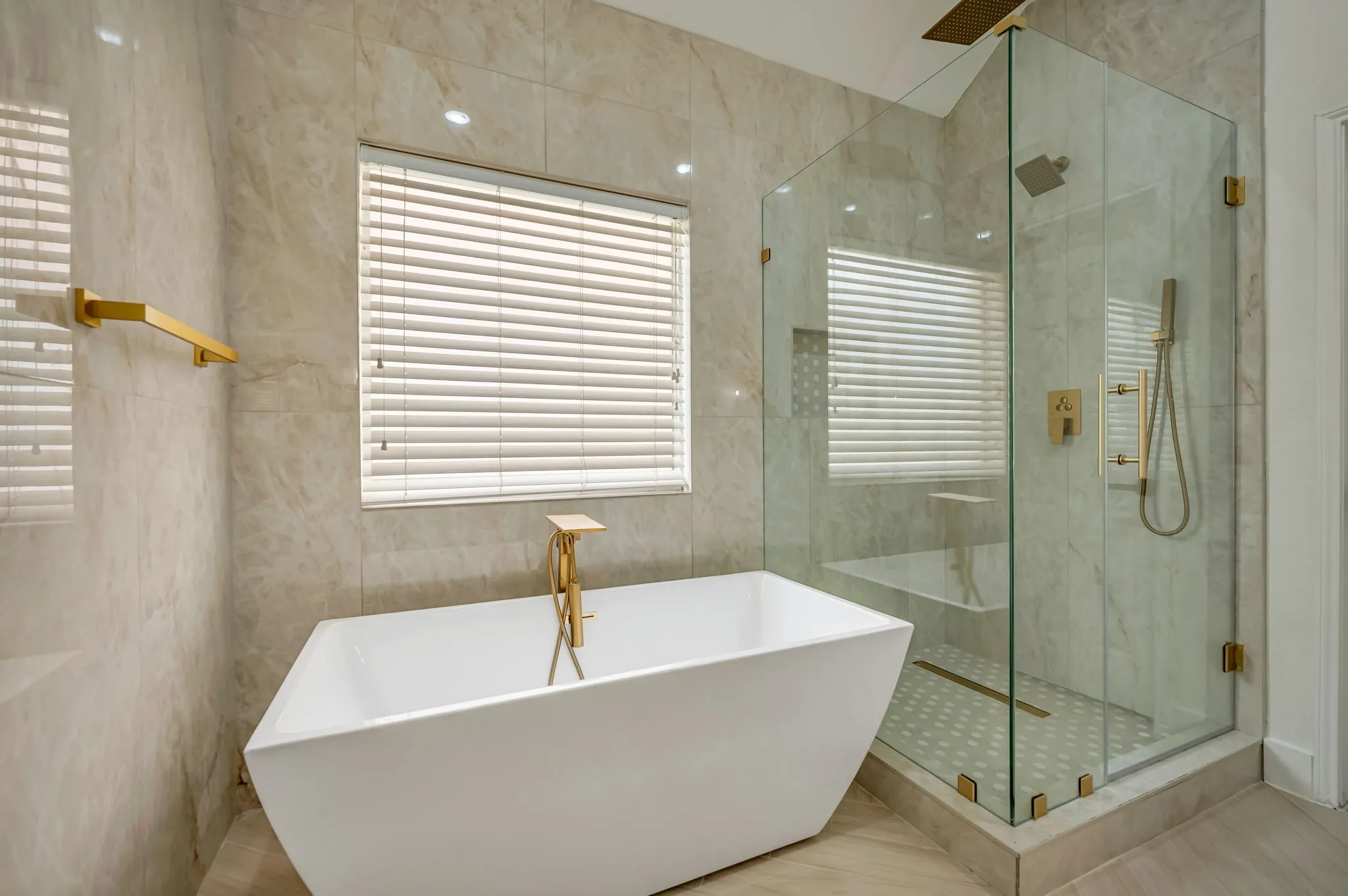 Freestanding soaking tub with gold-finish fixtures, a spacious glass-enclosed shower with a built-in bench, and floor-to-ceiling tile surround