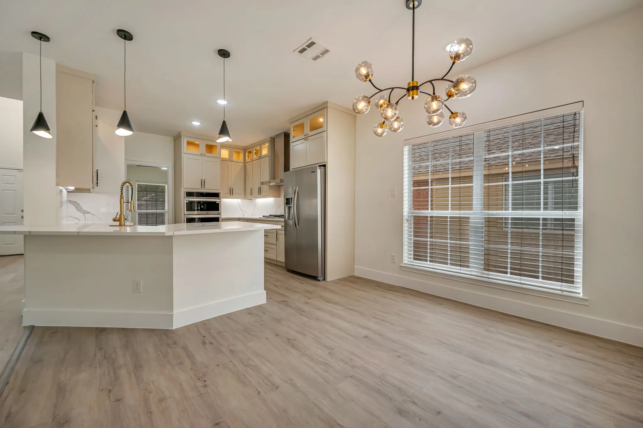 Kitchen featuring a gold vein quartz island, stainless steel appliances, light Luxury Vinyl Plank  flooring, recessed lighting, and a contemporary chandelier
