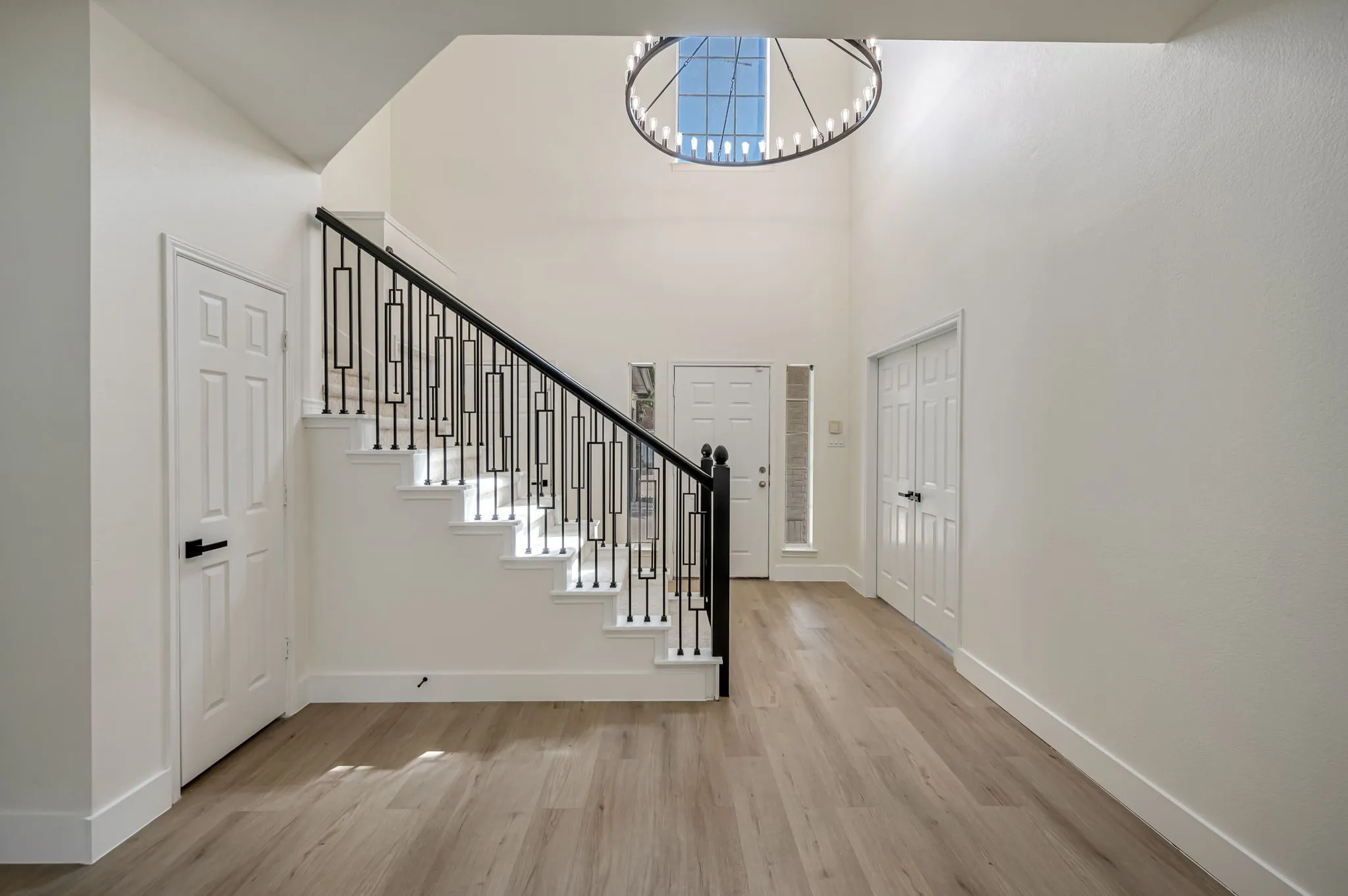 Grand foyer featuring Luxury Vinyl Plank  flooring, a contemporary chandelier, and a prominent staircase with decorative iron railings