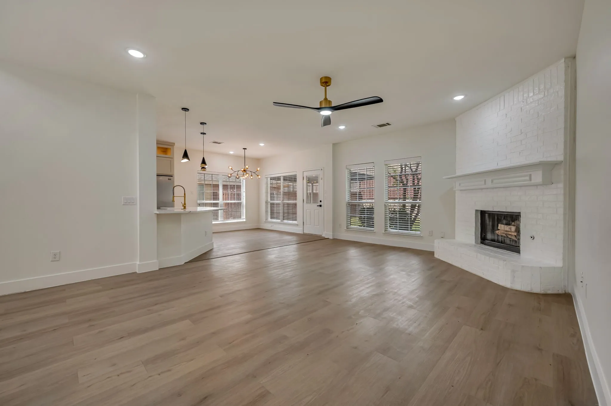 Expansive living area with Luxury Vinyl Plank  flooring, recessed lighting, and a corner brick fireplace with a mantle
