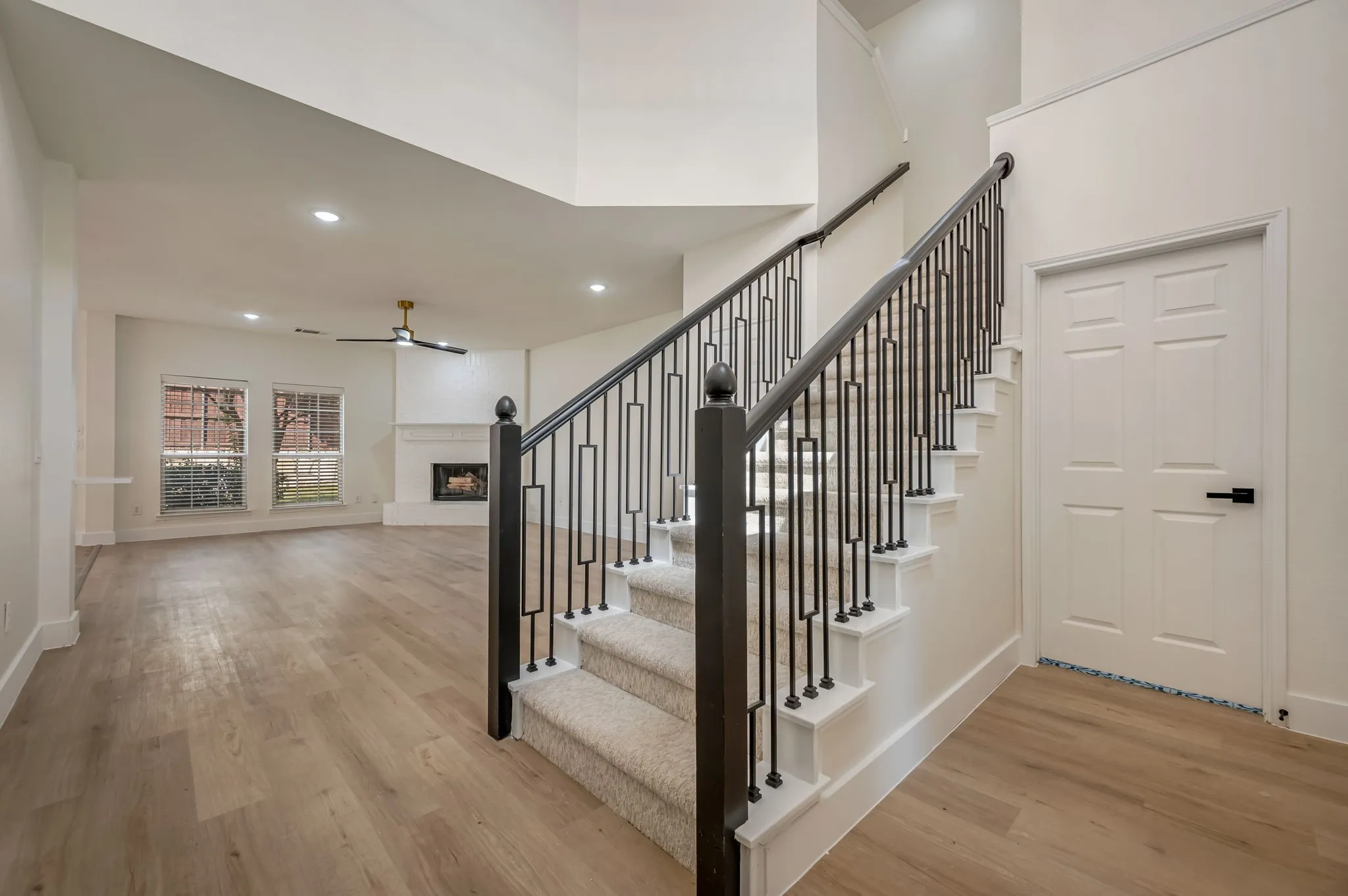 Luxury Vinyl Plank flooring, staircase with wrought iron balusters, carpeted stair treads, ceiling fan with integrated lighting, and a fireplace with a white mantel