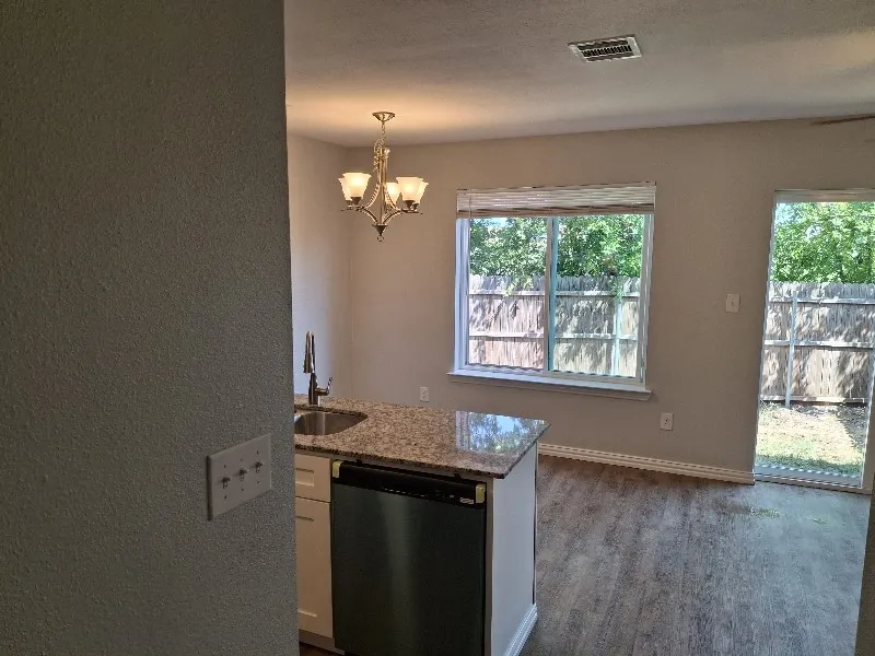 Kitchen with dishwasher, light stone counters, dark wood-style floors, a chandelier, and decorative light fixtures