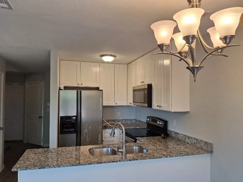Kitchen featuring dark stone counters, stainless steel appliances, white cabinetry, and pendant lighting