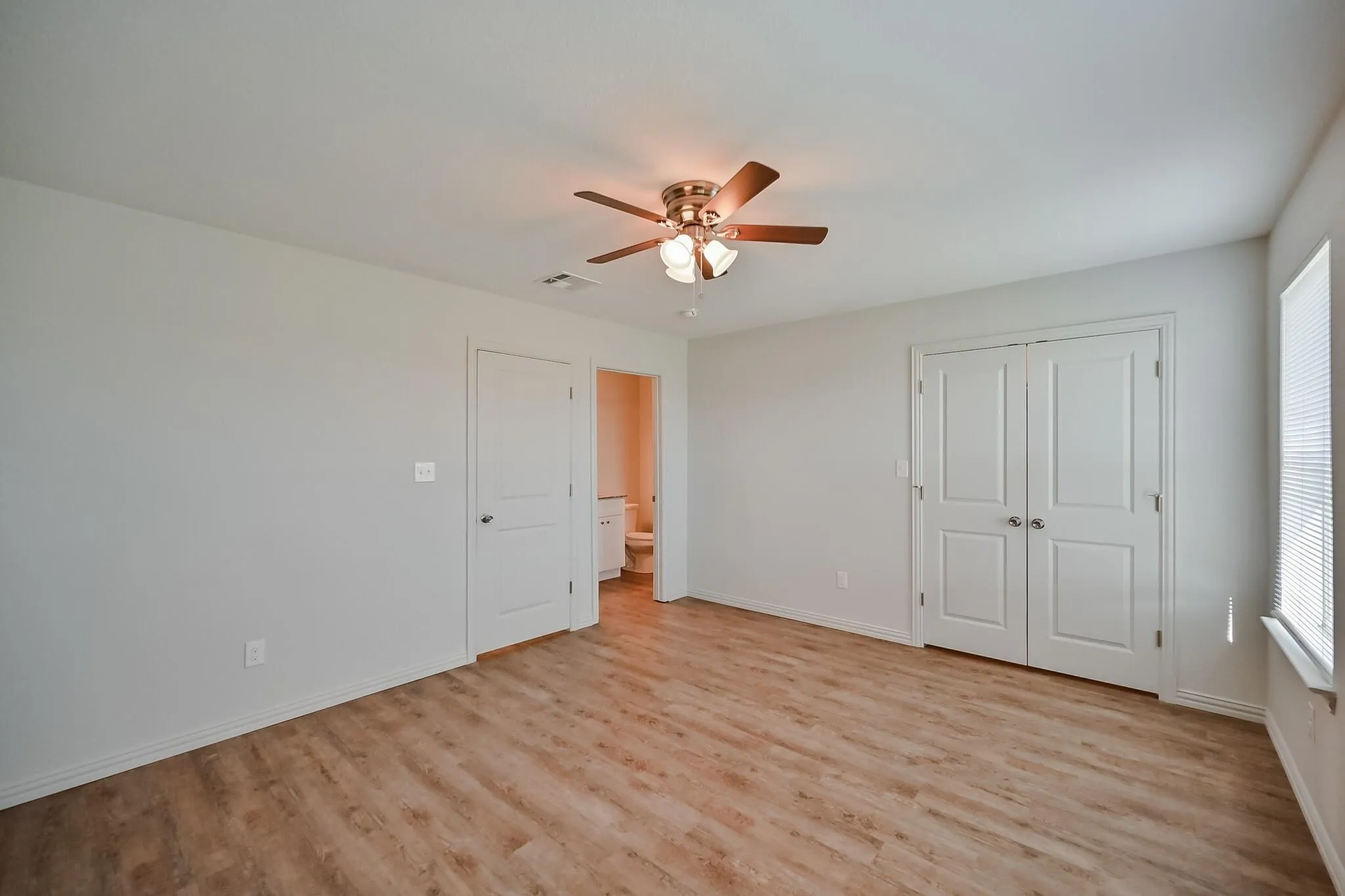 Unfurnished bedroom featuring light wood finished floors, a closet, connected bathroom, and ceiling fan