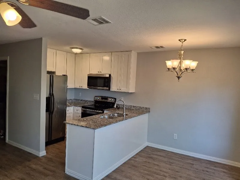 Kitchen with dark stone countertops, a peninsula, stainless steel appliances, white cabinetry, and hanging light fixtures