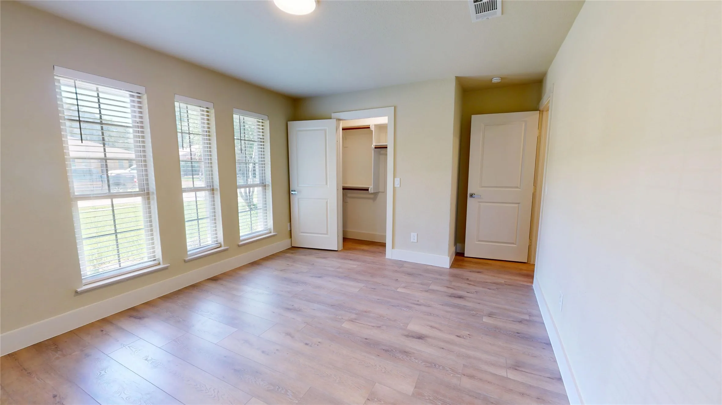Wood-finish flooring, three large windows with blinds, a built-in closet with shelving, and light-toned walls