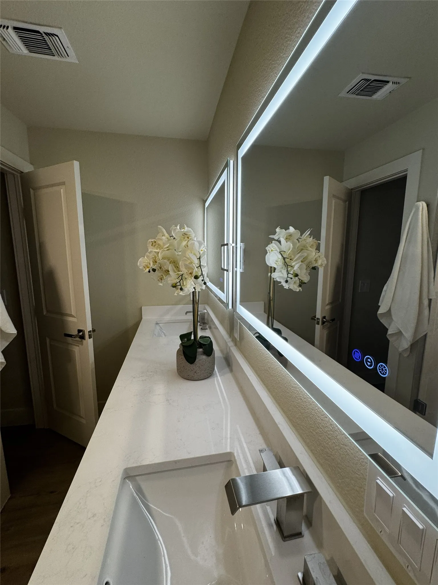 Dual vanity with integrated sinks and brushed nickel fixtures, illuminated mirrors, and a light-toned countertop