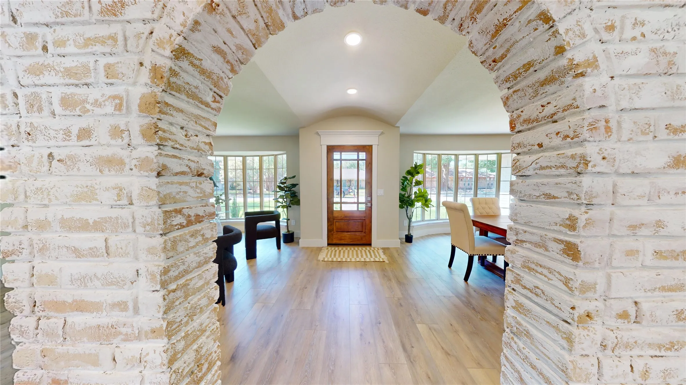 German Schmear brick archway leading to an entry hall with wood-finish flooring, a solid wood front door with glass panels, and multiple bay windows