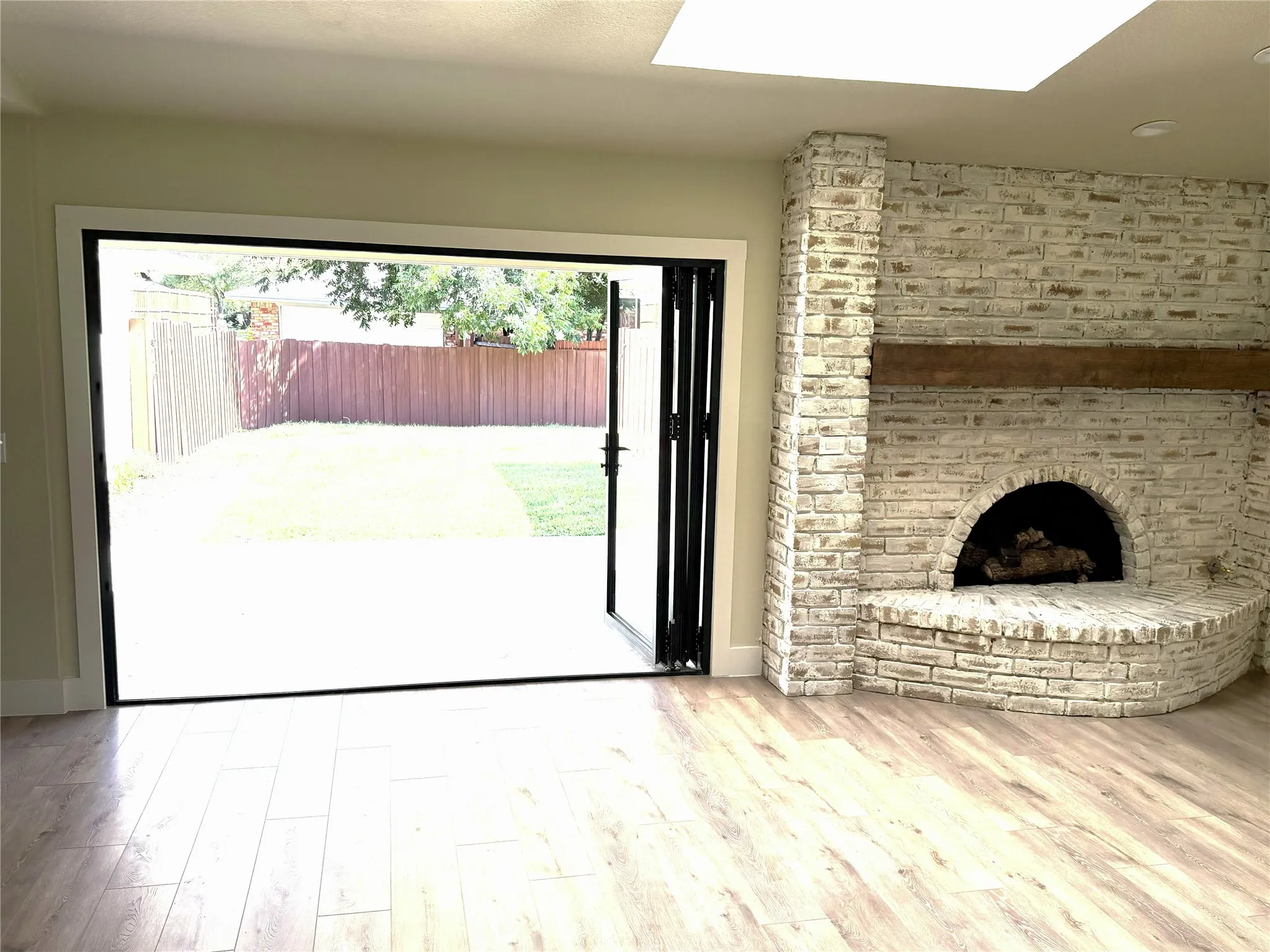 German Schmear brick fireplace with wood mantel, accordion glass doors- Open, wood-finish flooring, and a skylight