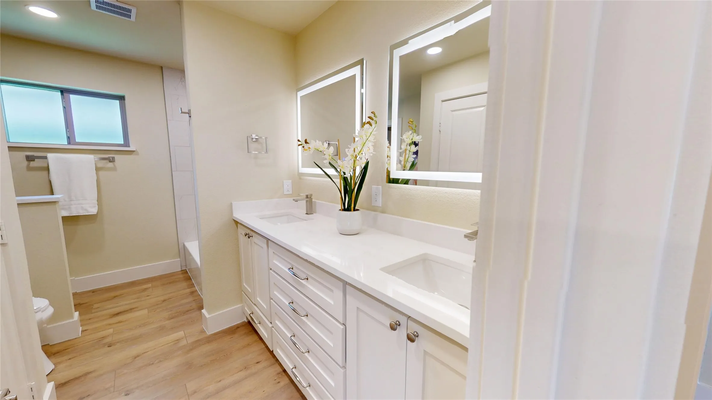 Dual vanity featuring white shaker cabinetry, integrated sinks, and illuminated mirrors