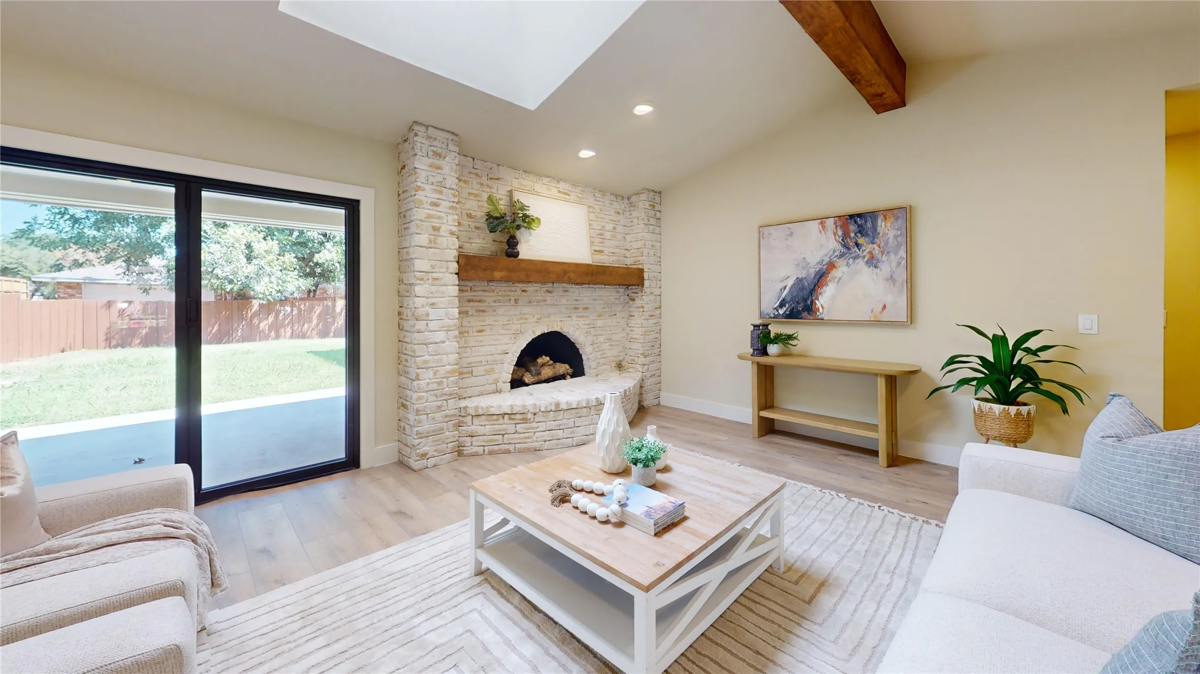 Vaulted ceilings with exposed wood beams, a German Schmear  brick fireplace with a wood mantel, wood-finish flooring, and sliding glass doors opening to a concrete patio and a private fenced yard