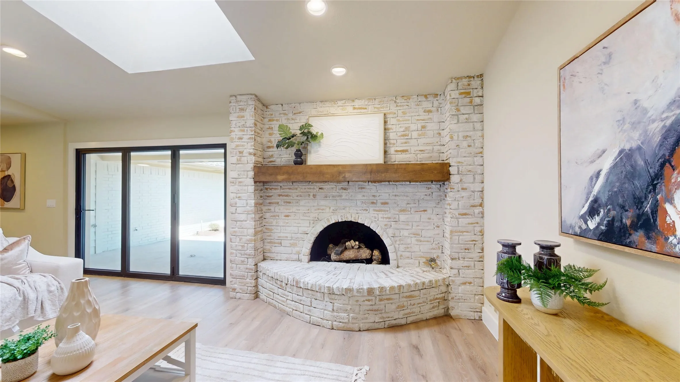 Light wood-finish flooring, German Schmear brick fireplace with hearth and wood mantel, recessed lighting, and a skylight