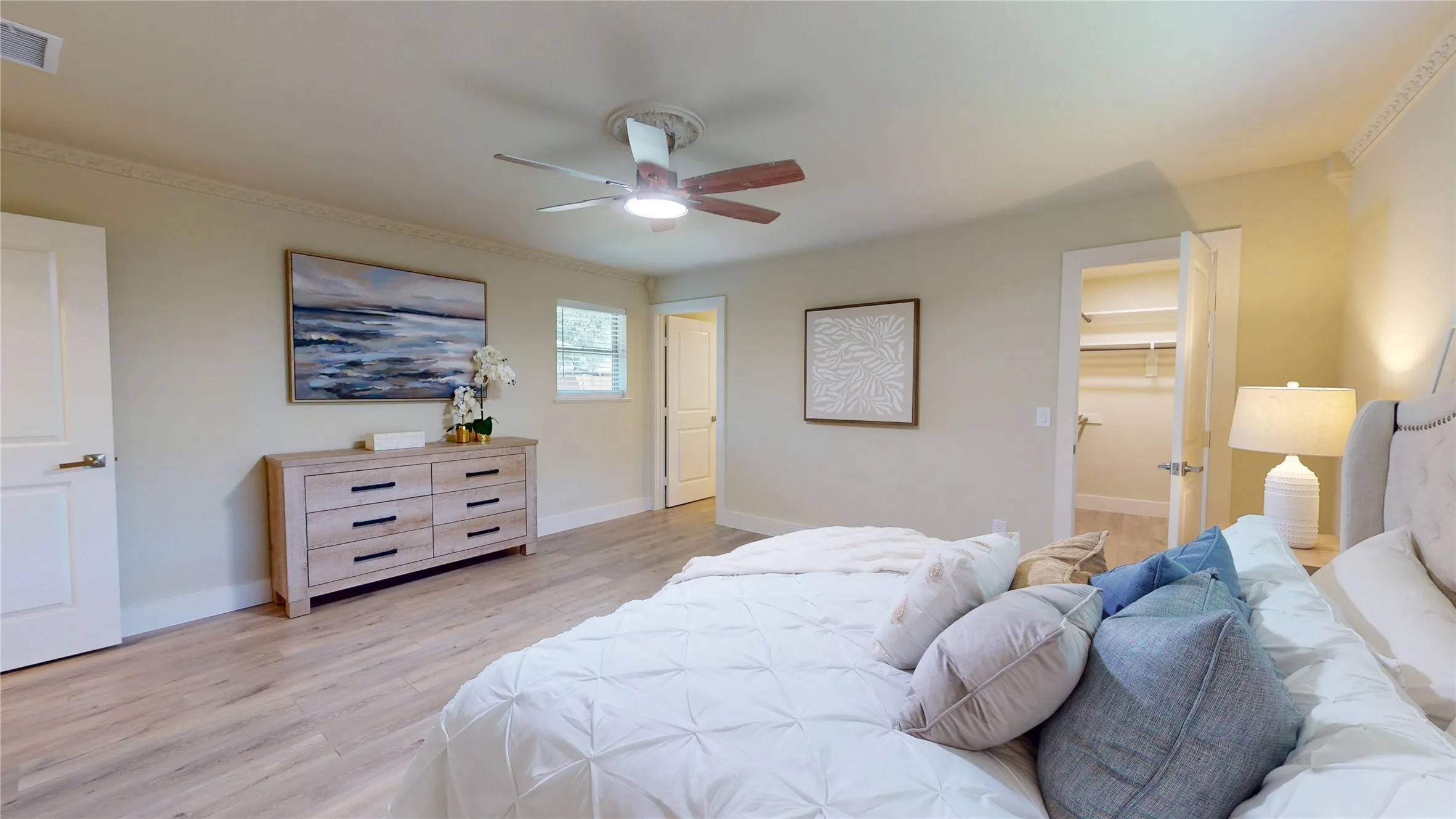 Wood-finish flooring throughout, ceiling fan with integrated lighting, crown molding, and a walk-in closet with built-in shelving
