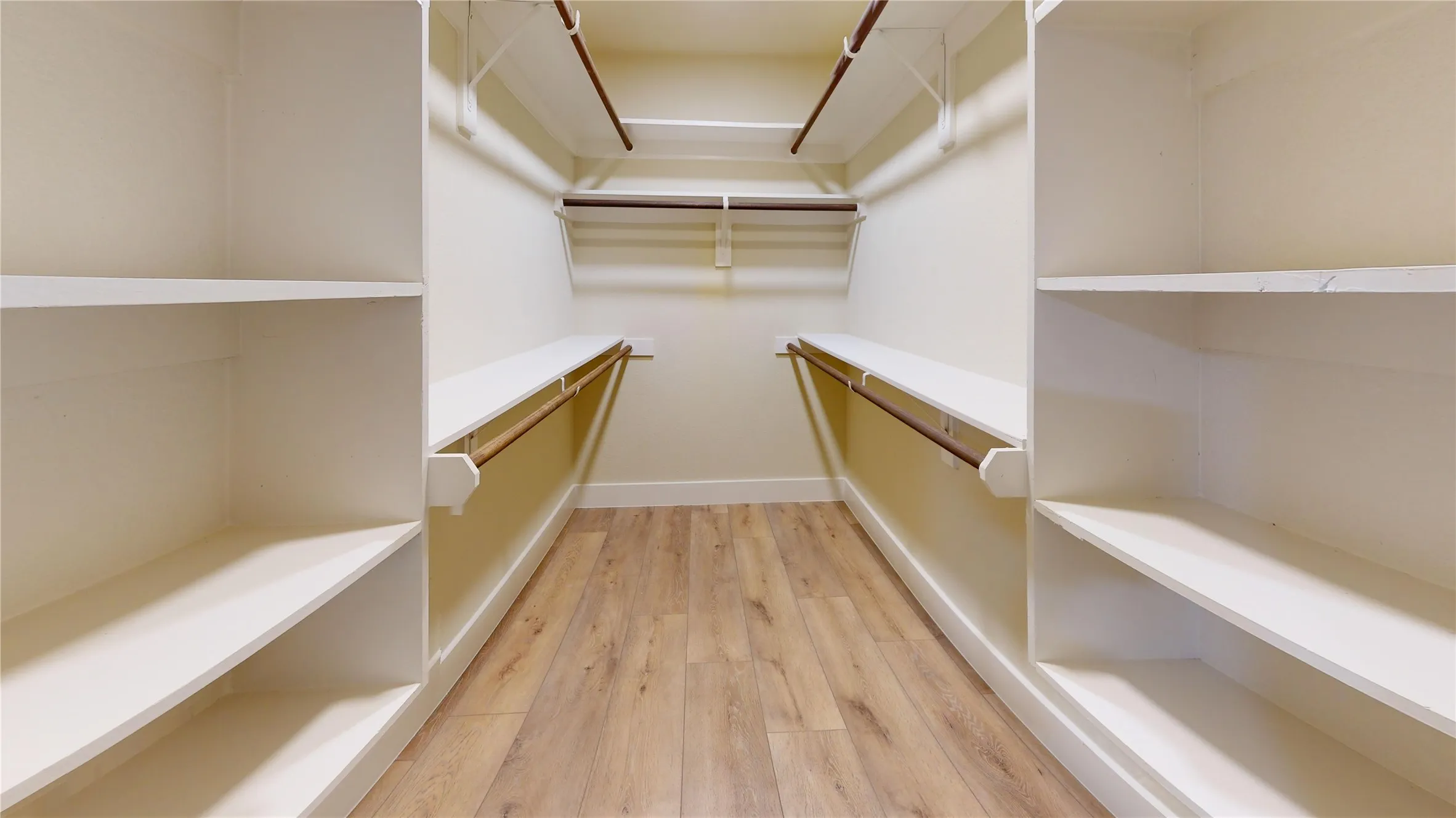Walk-in closet with wood-finish flooring, built-in shelving, and multiple hanging rods