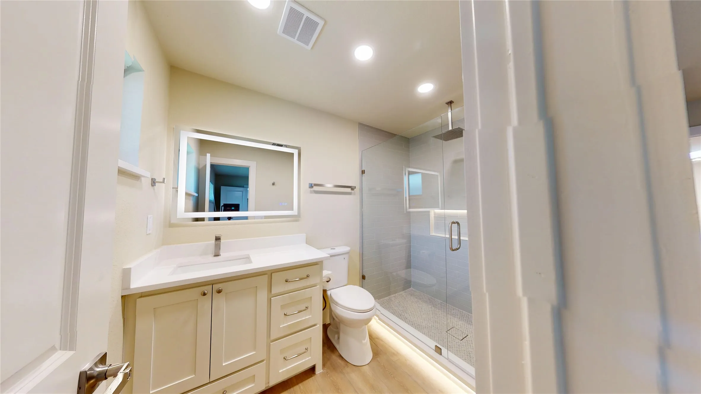 Wood-finish flooring, single vanity with light-toned countertop, illuminated mirror, glass-enclosed shower, and recessed lighting in 2nd primary bath