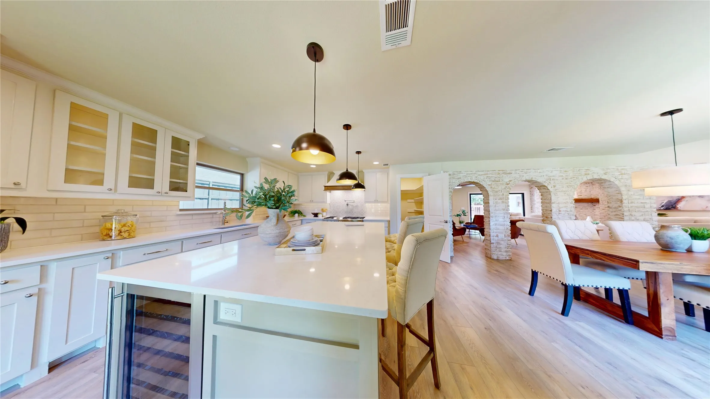 Expansive kitchen island with a built-in beverage cooler, white cabinetry, subway tile backsplash, and wood-finish flooring