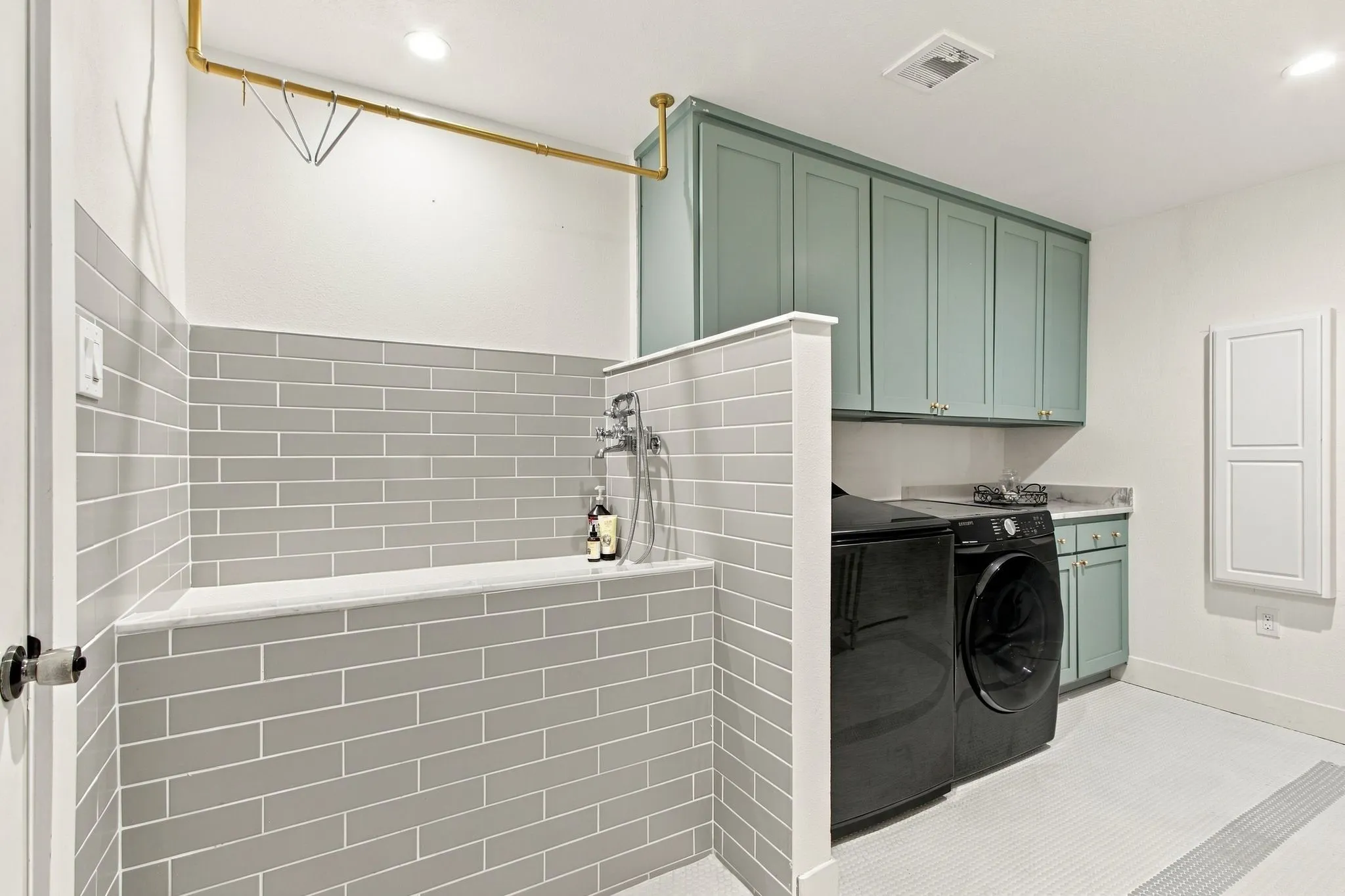 Utility room featuring a tiled dog washing station with an overhead drying rack, custom cabinetry, a built-in sink, and tile flooring