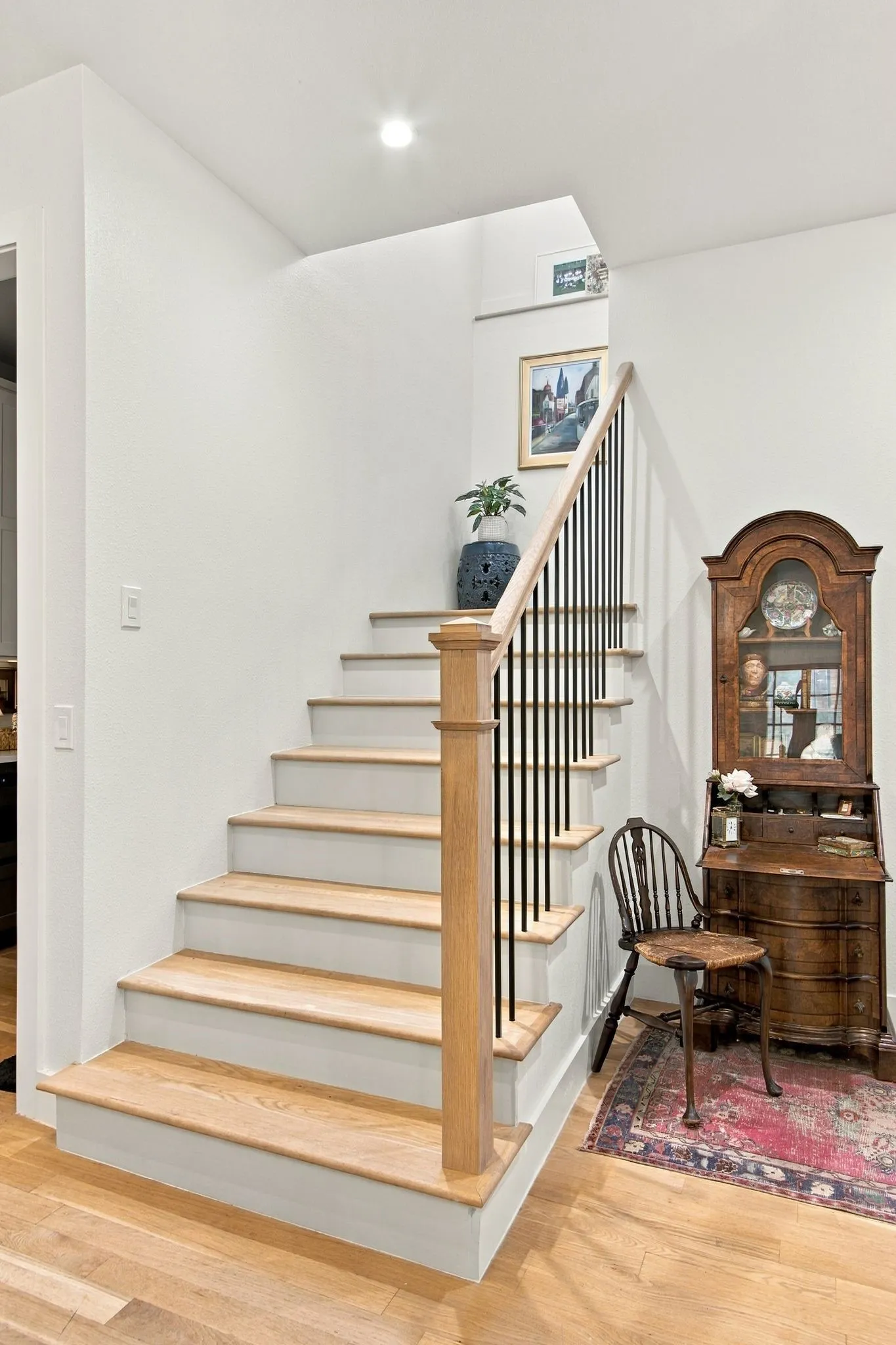 Hardwood flooring and staircase with natural wood treads, white risers, and a black metal spindle railing