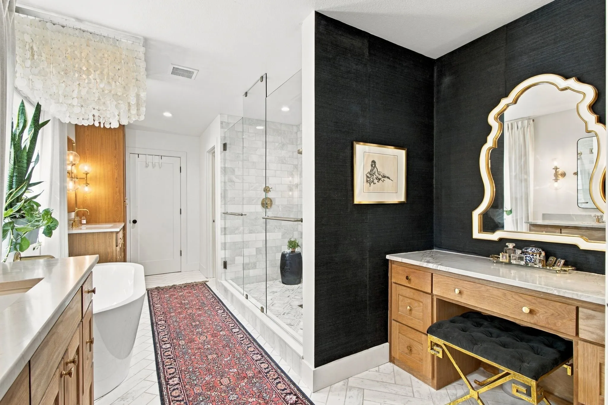 Glass-enclosed shower with subway tile surround, standalone soaking tub, dual vanities with integrated sinks, wood-finish cabinetry, and a dedicated vanity desk with a stone countertop