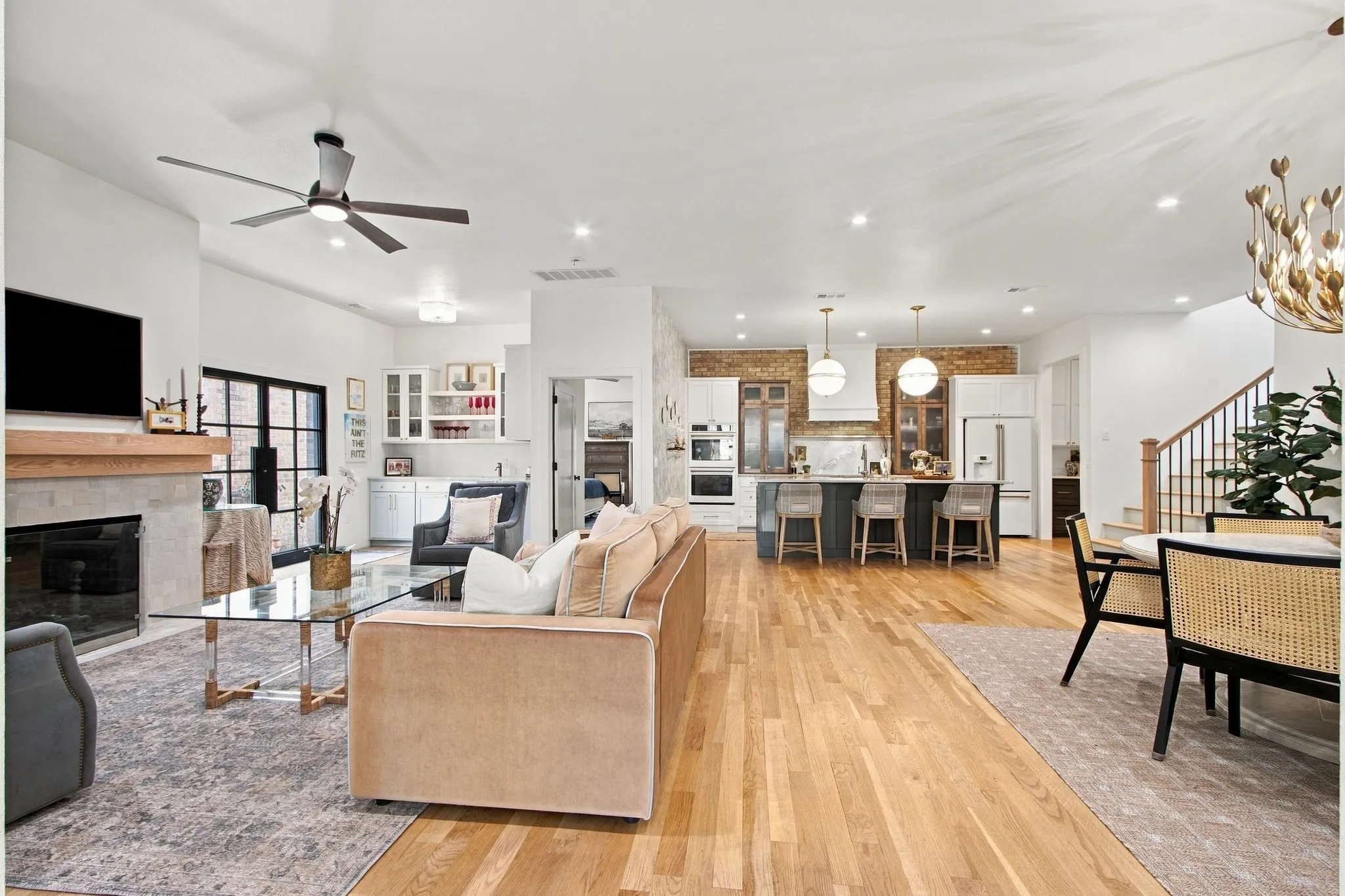 Hardwood flooring throughout, a modern fireplace with a wood mantel, a kitchen island with pendant lighting, a built-in dry bar with upper glass cabinetry, and a staircase with wood newel posts and railings