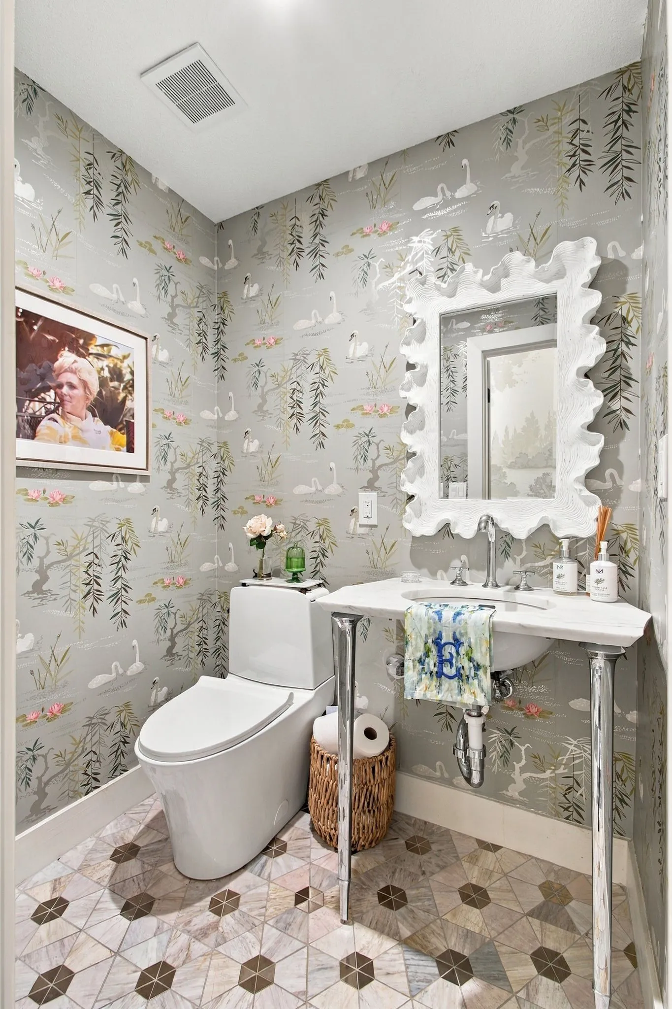 Patterned wallpaper, geometric tile flooring, white pedestal sink, white toilet, decorative wall mirror