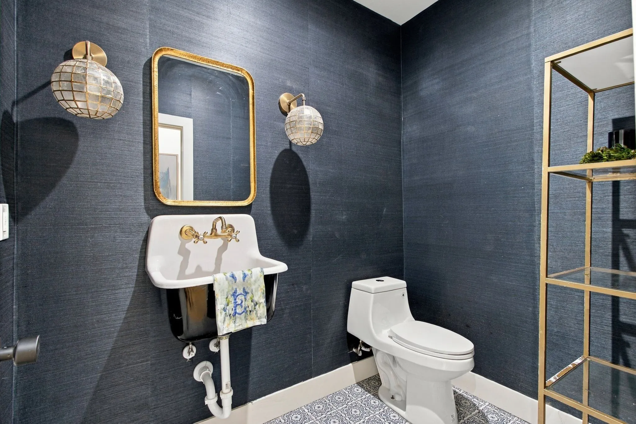 Textured wall covering, decorative floor tile, wall-mounted sink, gold-framed mirror, and gold-finish shelving