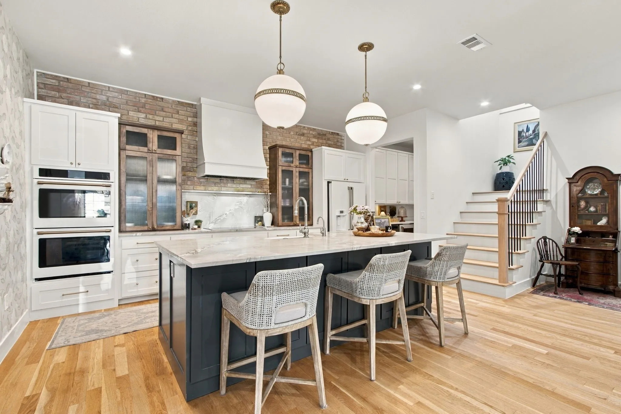 Kitchen featuring a central island with countertop seating, integrated double ovens, brick accent wall, and light wood-finish flooring