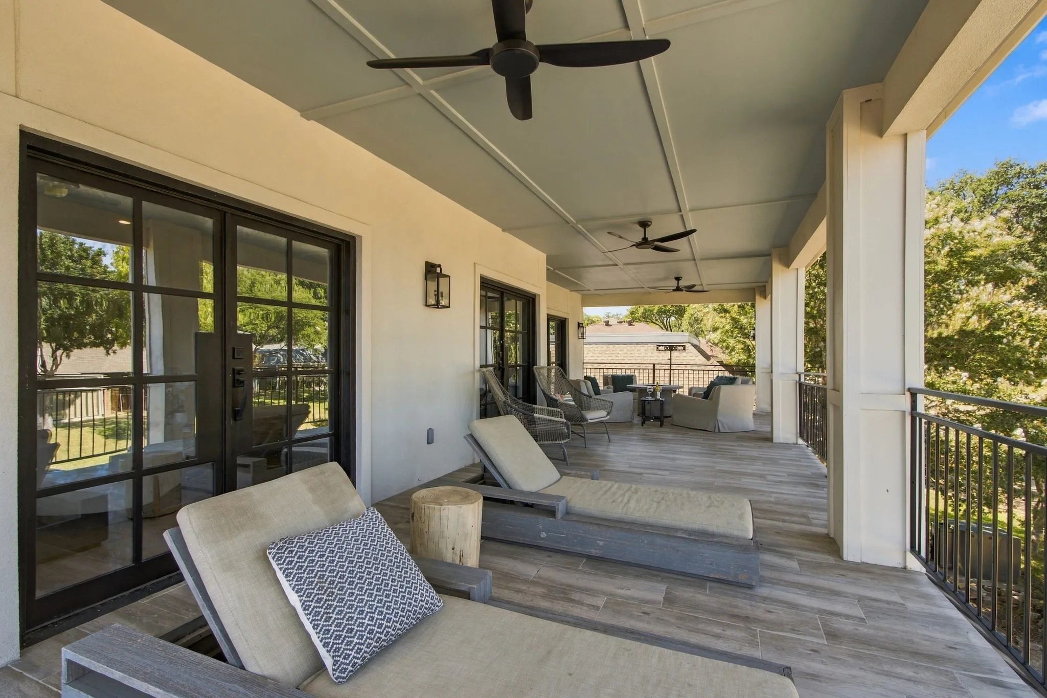 Expansive covered patio featuring wood-look tile flooring, a coffered ceiling with integrated fans, and a black wrought iron railing