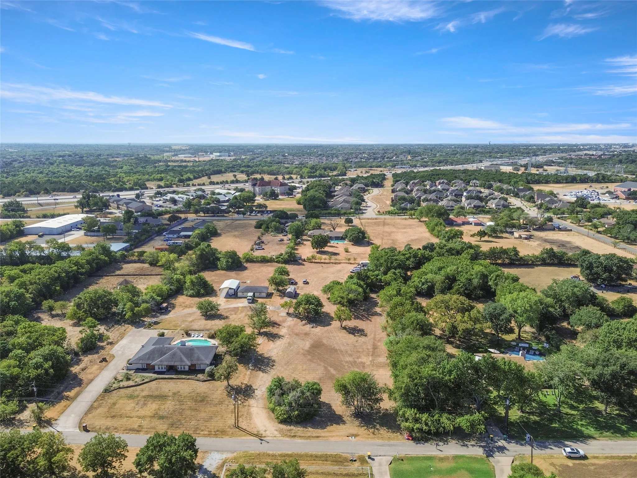 Expansive property featuring a single-story residence, private swimming pool, mature trees, and a long paved driveway