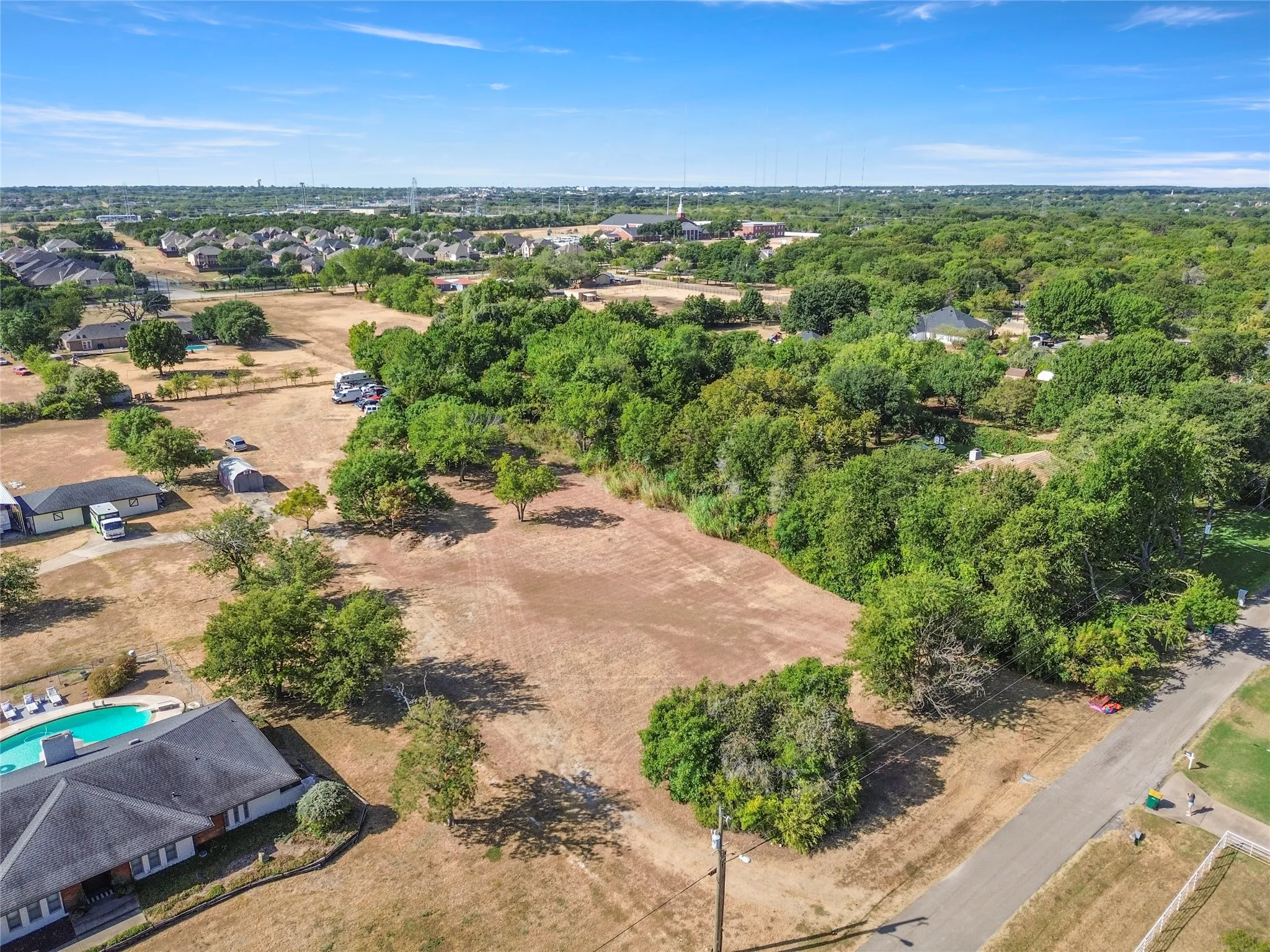 Cleared land parcel with mature trees and paved road frontage
